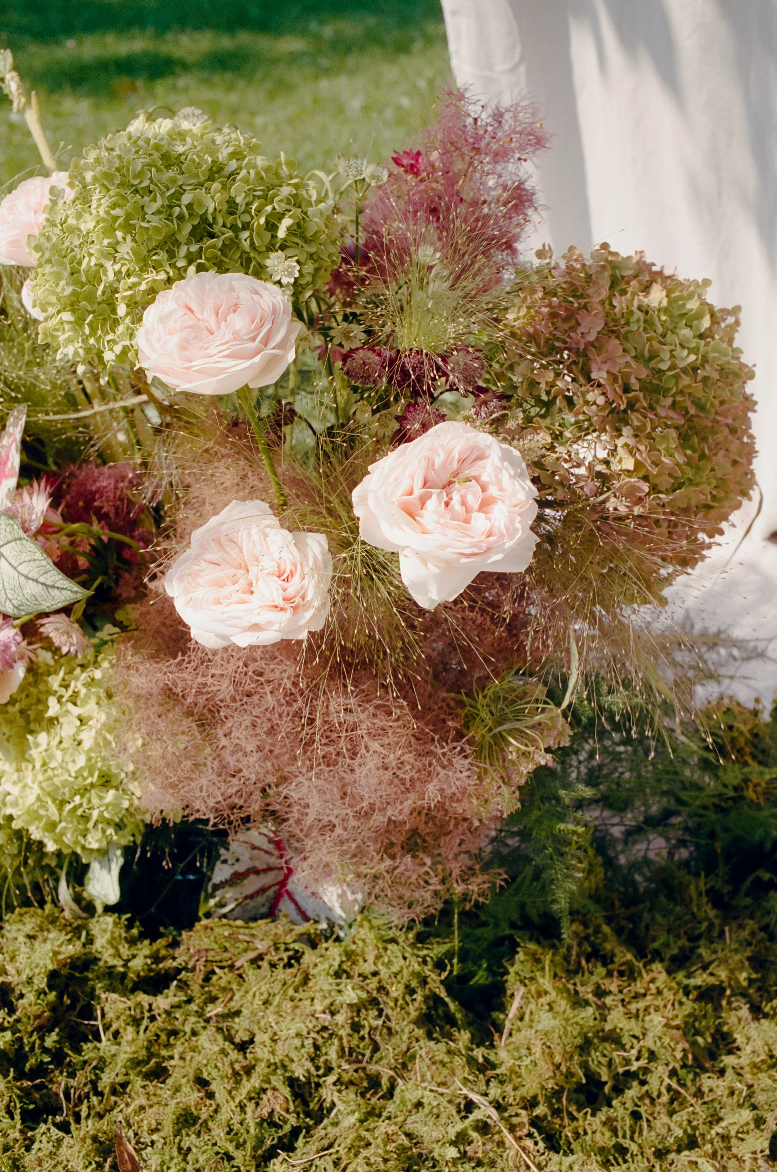 A floral arrangement with pink roses, green hydrangeas, and other flowers on mossy ground.