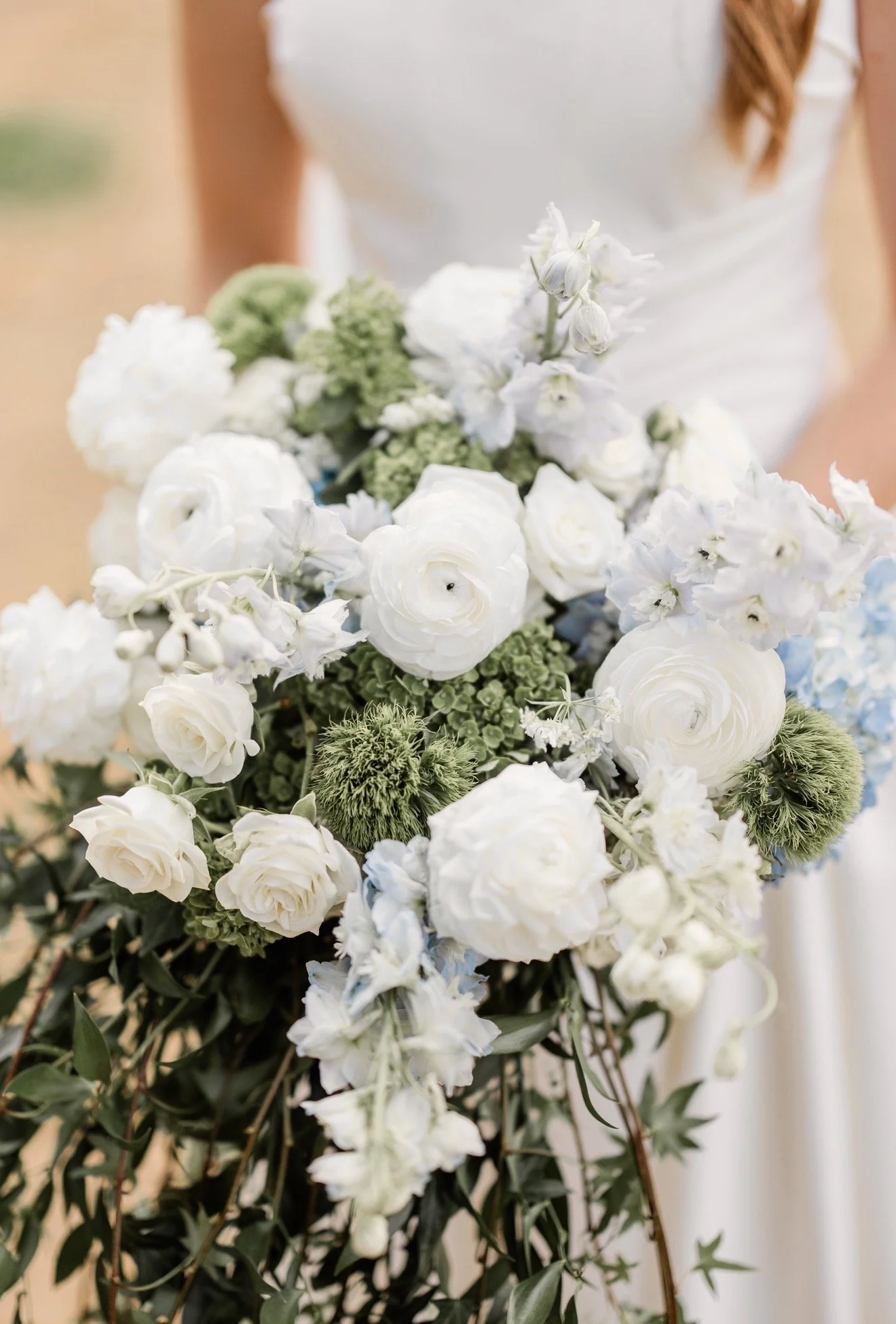 A woman holding a bouquet of white and green flowers, with part of her white dress visible and her brown hair also visible.