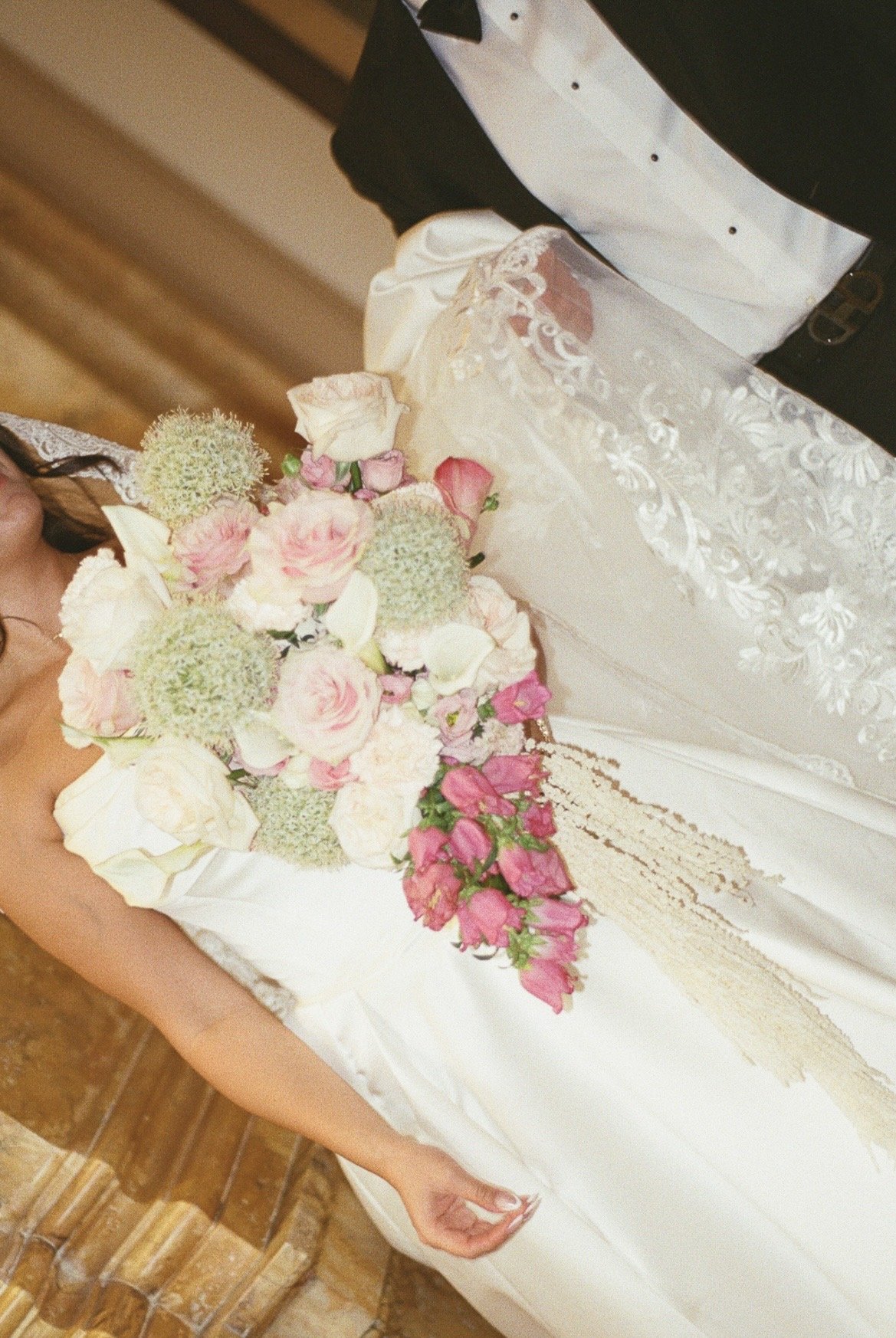 A bride in a wedding dress holding a bouquet of flowers, standing next to a groom in a tuxedo.