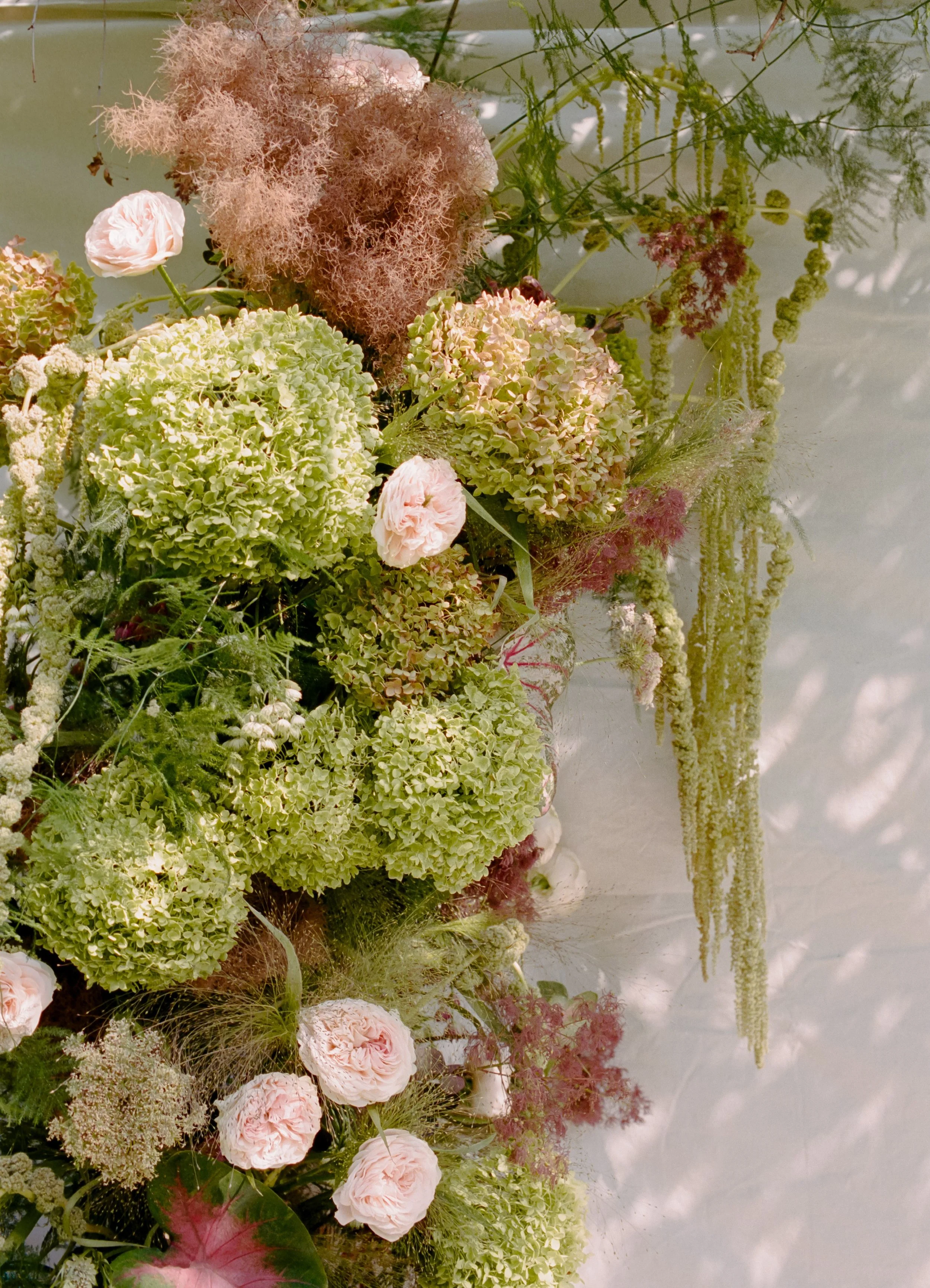 A floral arrangement with pink roses, green hydrangeas, and other pink and green flowers and foliage, reflected on water at a garden or outdoor setting.