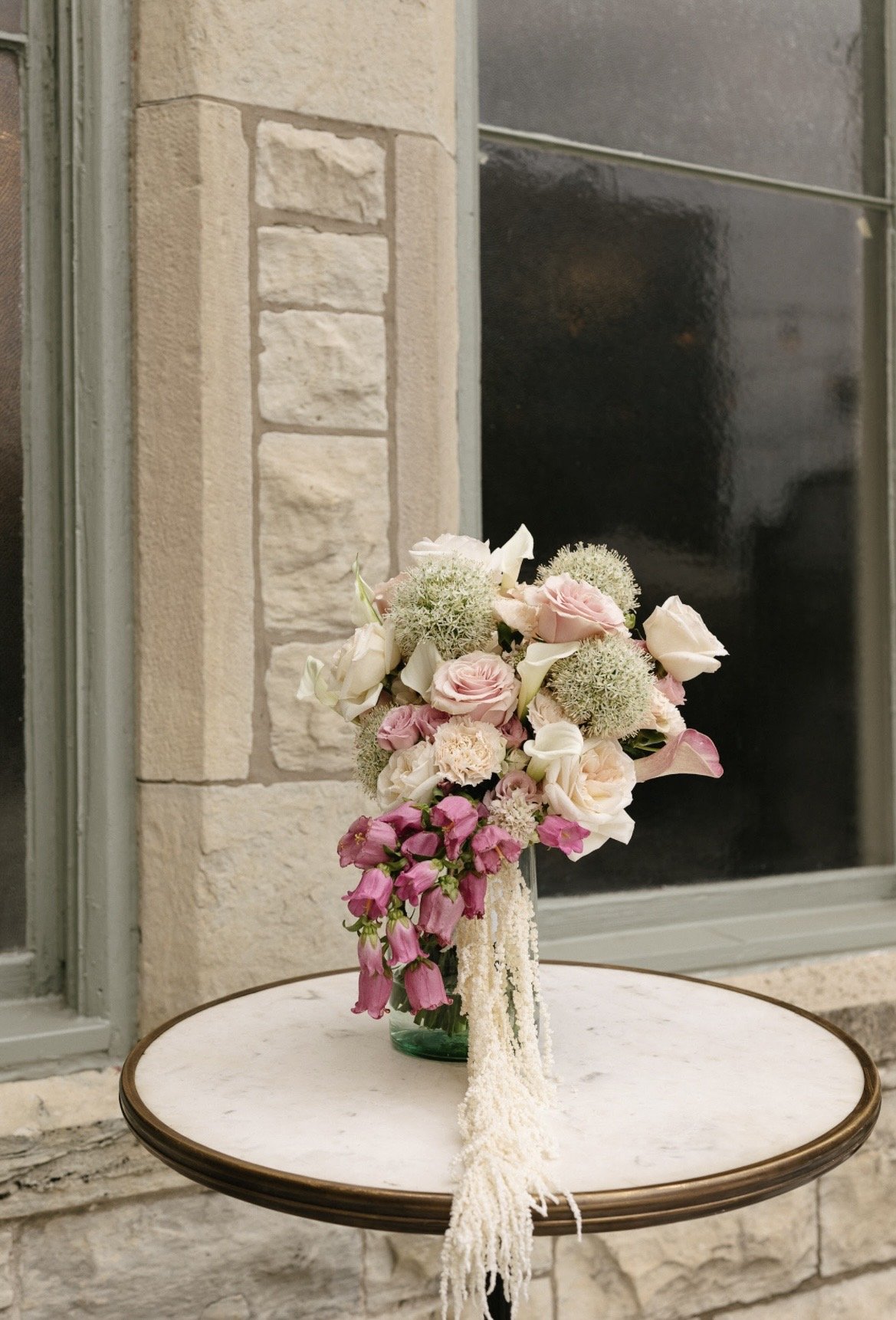A floral arrangement with white and pink flowers on a small round table outside near a stone building.