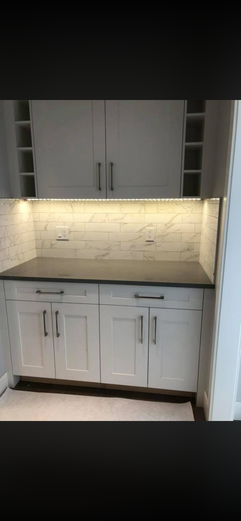 Modern kitchen cabinetry and countertop with under-cabinet lighting and tiled backsplash.