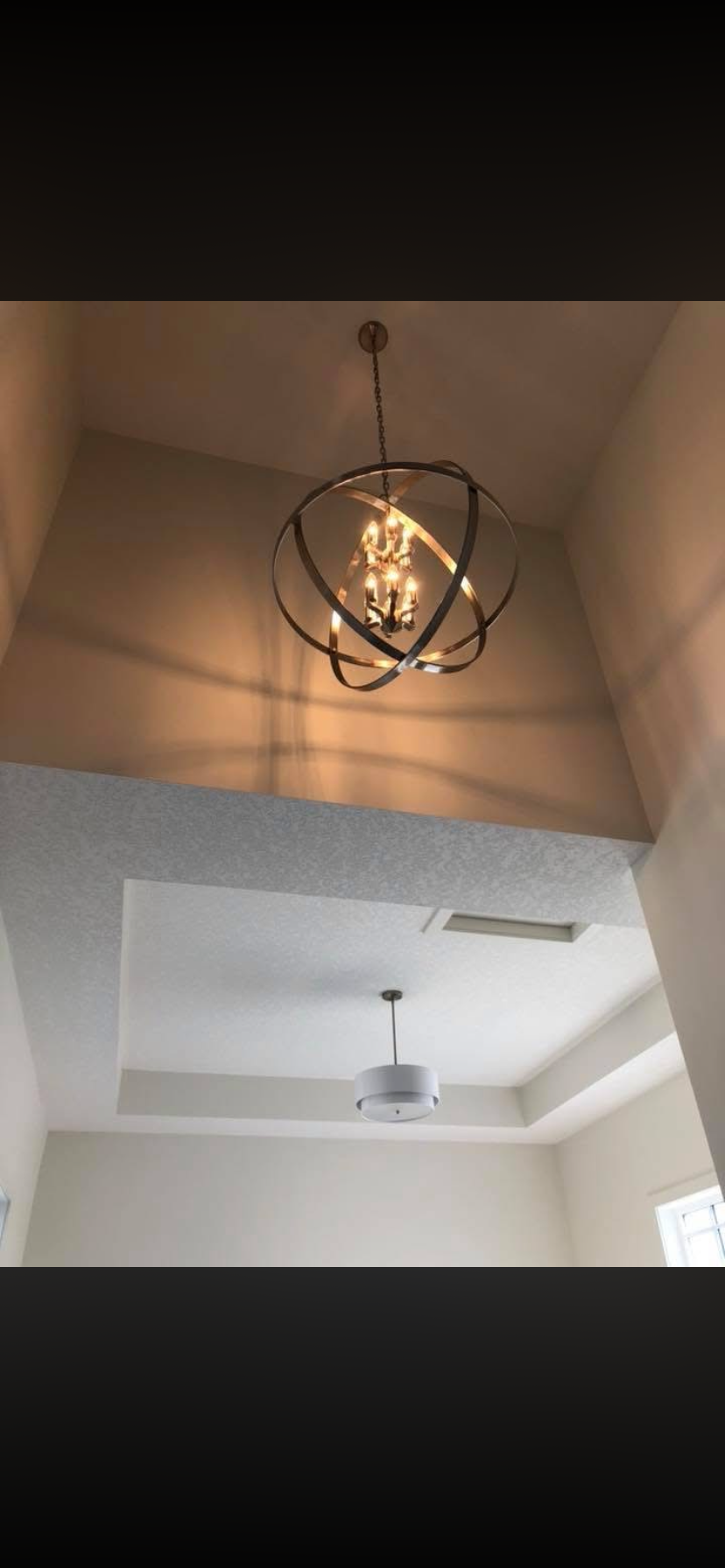 Two ceiling lights, one with a chandelier and modern sculpture pendant, and the other with a white drum-shaped fixture, installed in a room with white walls and ceiling.