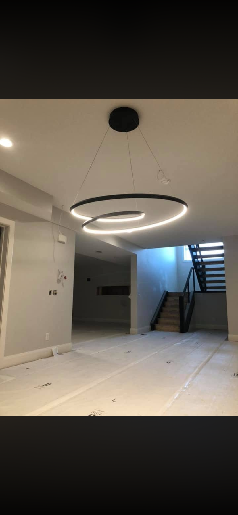 Empty room under renovation with modern circular pendant lighting and black staircase.