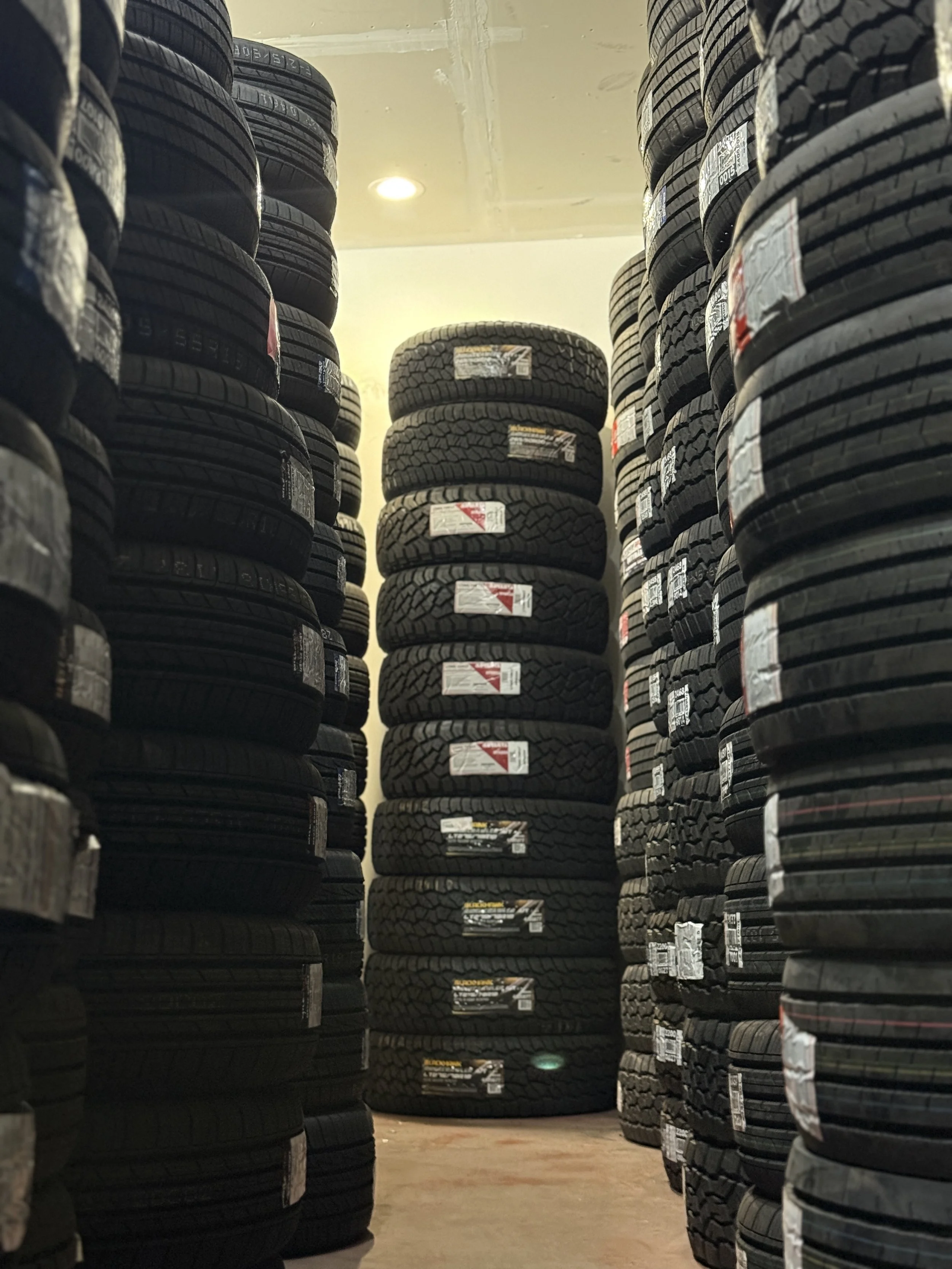 Stacks of new tires arranged vertically in a storage area, with labels and some labels with red and yellow markings visible on the tires.