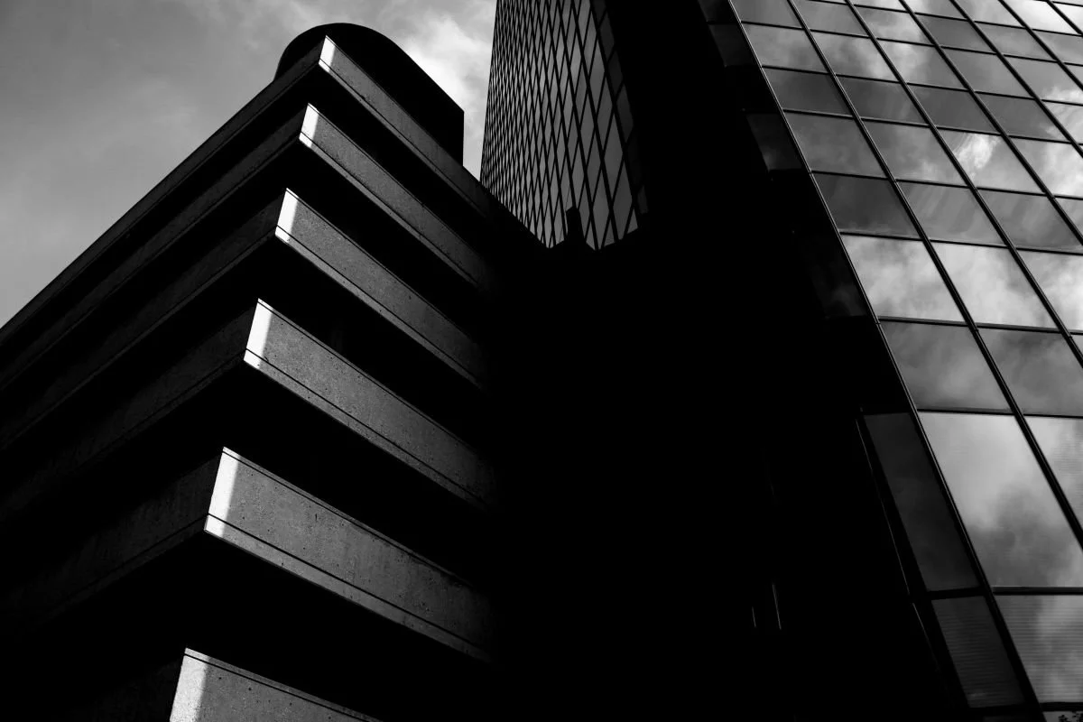 A black and white architectural photo looking up at a brick and stone structure next to a large glass building in downtown Winnipeg, Manitoba.