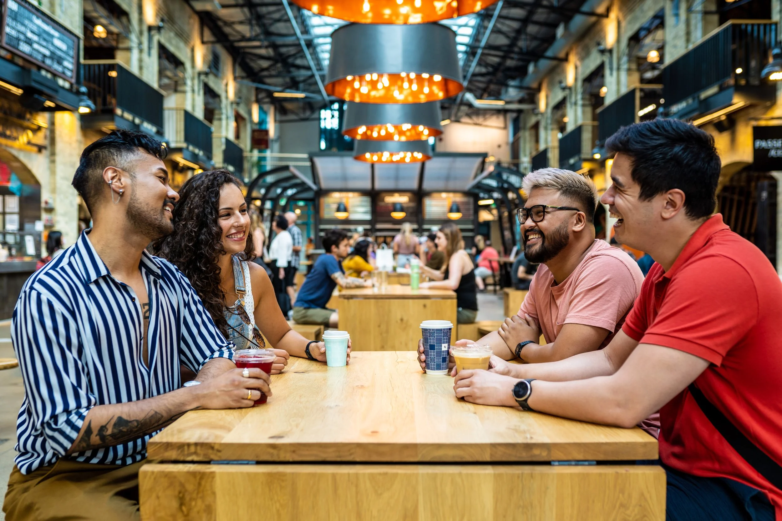 A group of friends laughing and drinking coffee together inside The Forks in Winnipeg, Manitoba