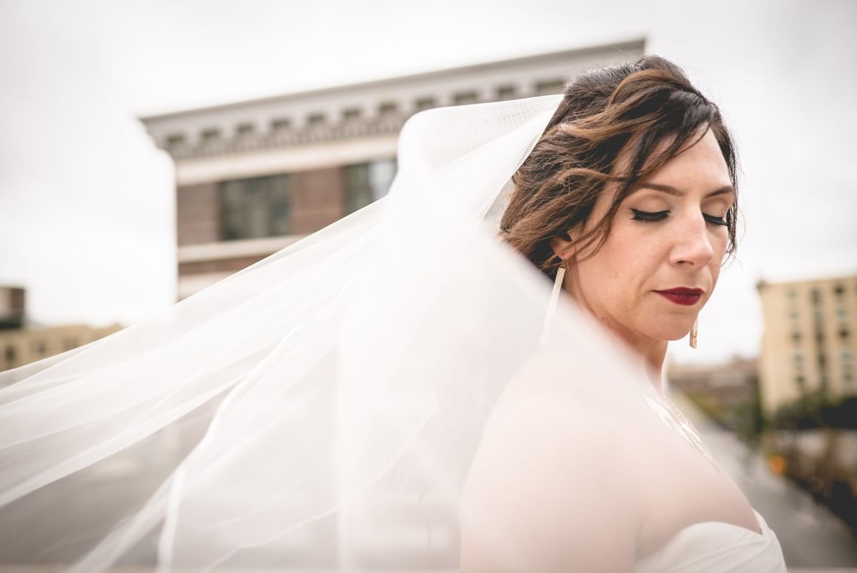Bride closing her eyes with a white veil flowing in the wind in the Exchange District of Winnipeg, Manitoba