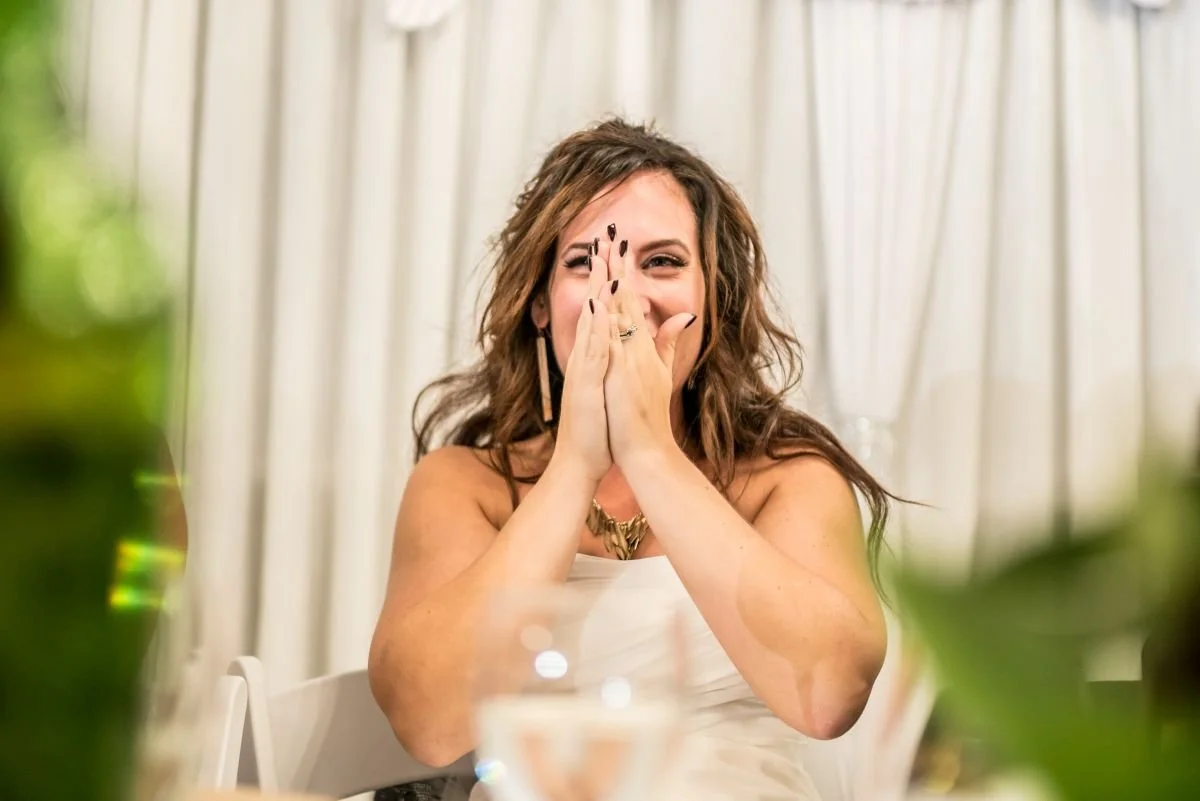 A bride covering her face while laughing at the head table at Ashgrove Acres in Manitoba.