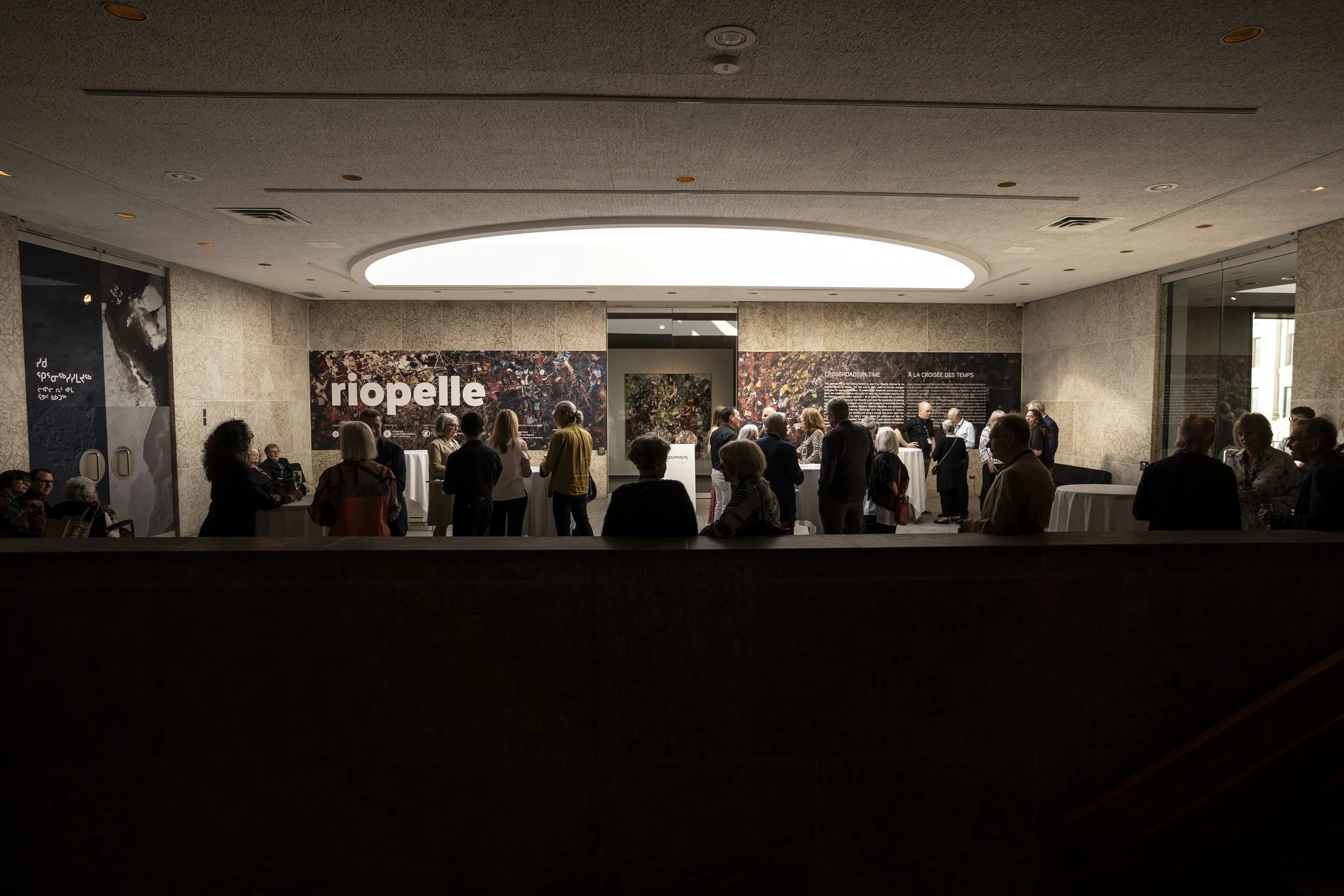 A large group of people gathering in Eckhardt Hall under the third-floor skylight at the Winnipeg Art Gallery, waiting for the Riopelle exhibit to open