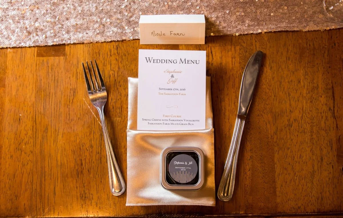 A detailed rustic flat lay of an elegant wedding reception table setting featuring a custom menu card at The Saskatoon Farm, captured during destination wedding in Alberta, captured by a Winnipeg wedding photographer.