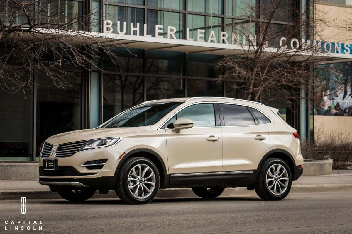A commercial automotive photograph of a cream-colored Lincoln MKC luxury SUV parked on an urban street in front of the Buhler Learning Commons building, shot for a Capital Lincoln and Lincoln Canada campaign in Winnipeg.