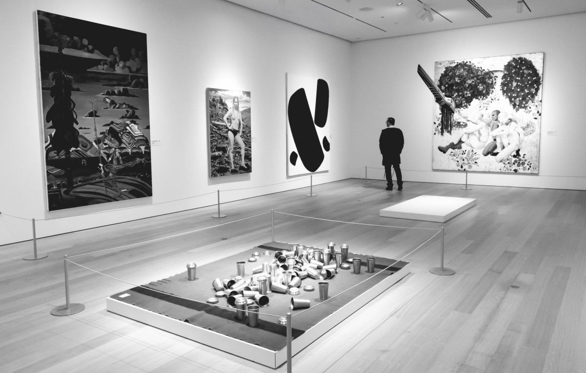 A black and white photo of a man standing in the far corner of a gallery room inside an art museum in Whistler, British Columbia.