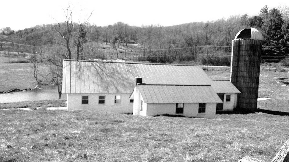 Black and white photo of a rural farm with a house and a silo, with trees and a river in the background.