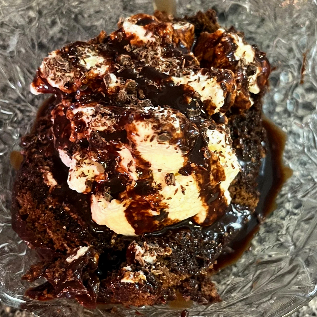 A decadent chocolate swiss roll dessert topped with homemade whipped cream, chocolate shavings, and drizzled with chocolate sauce
