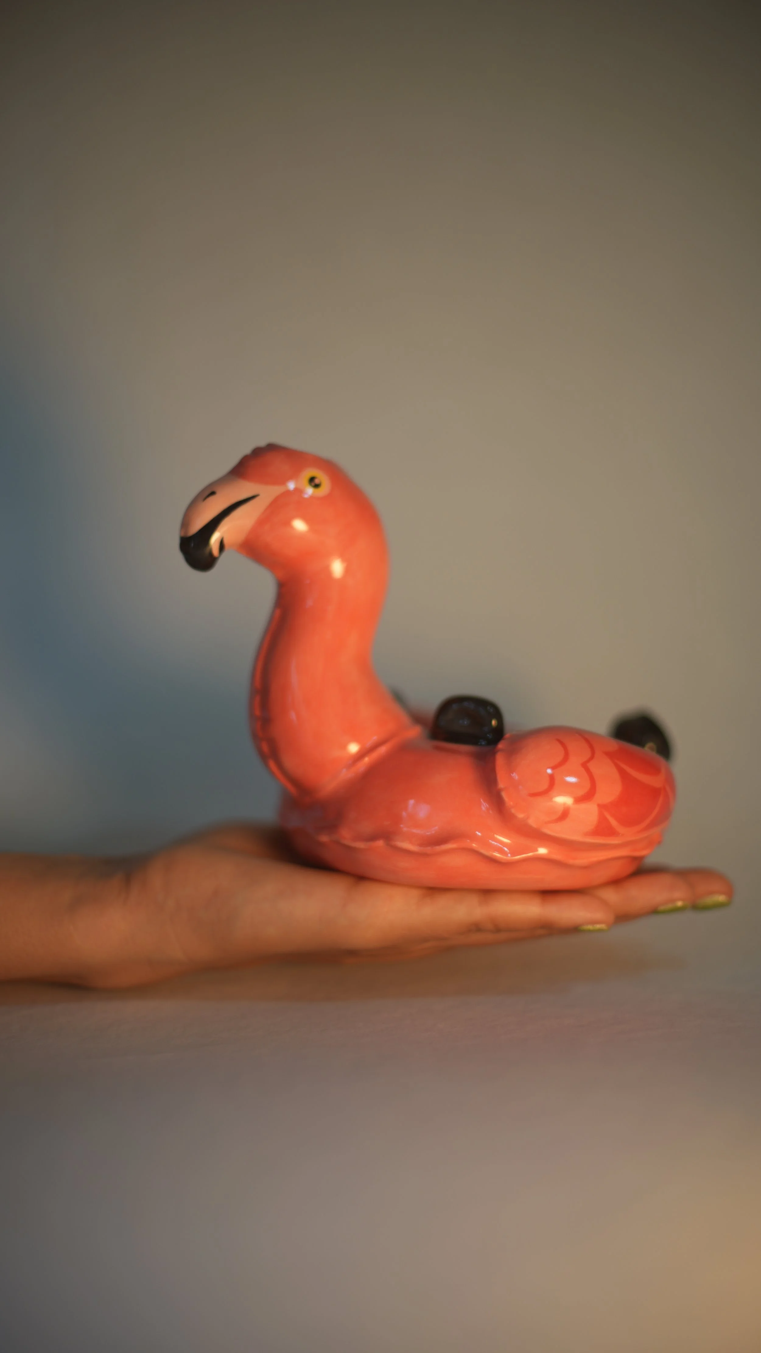 Pink flamingo-shaped ceramic water bong held in a person's hand against a neutral background.