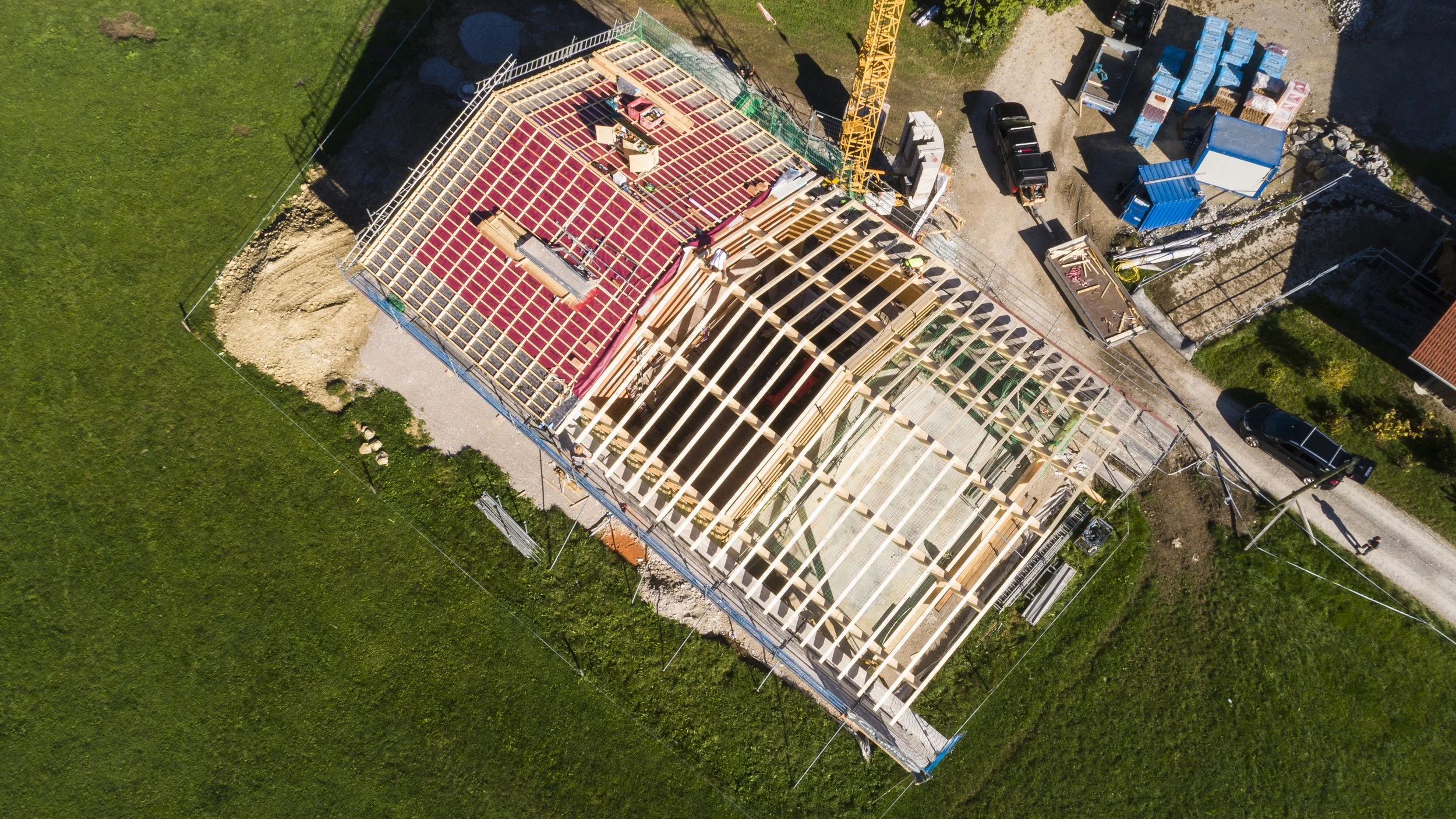 Vogelansicht eines Baugerüsts für ein Gebäude mit einem abgedeckten Dach, umgeben von grünem Rasen und Baustellenequipment.