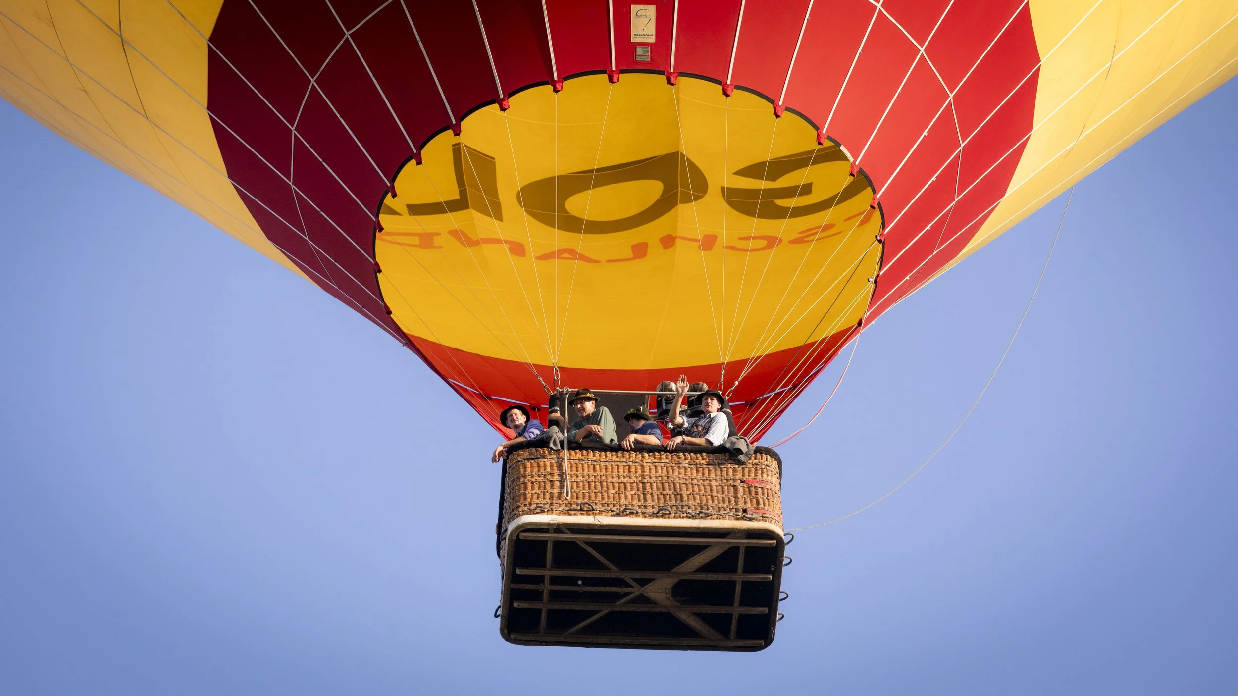 Heißluftballon mit gelbem und roten Segel, fahrbare Korbfahne mit Passagieren, in blauen Himmel.
