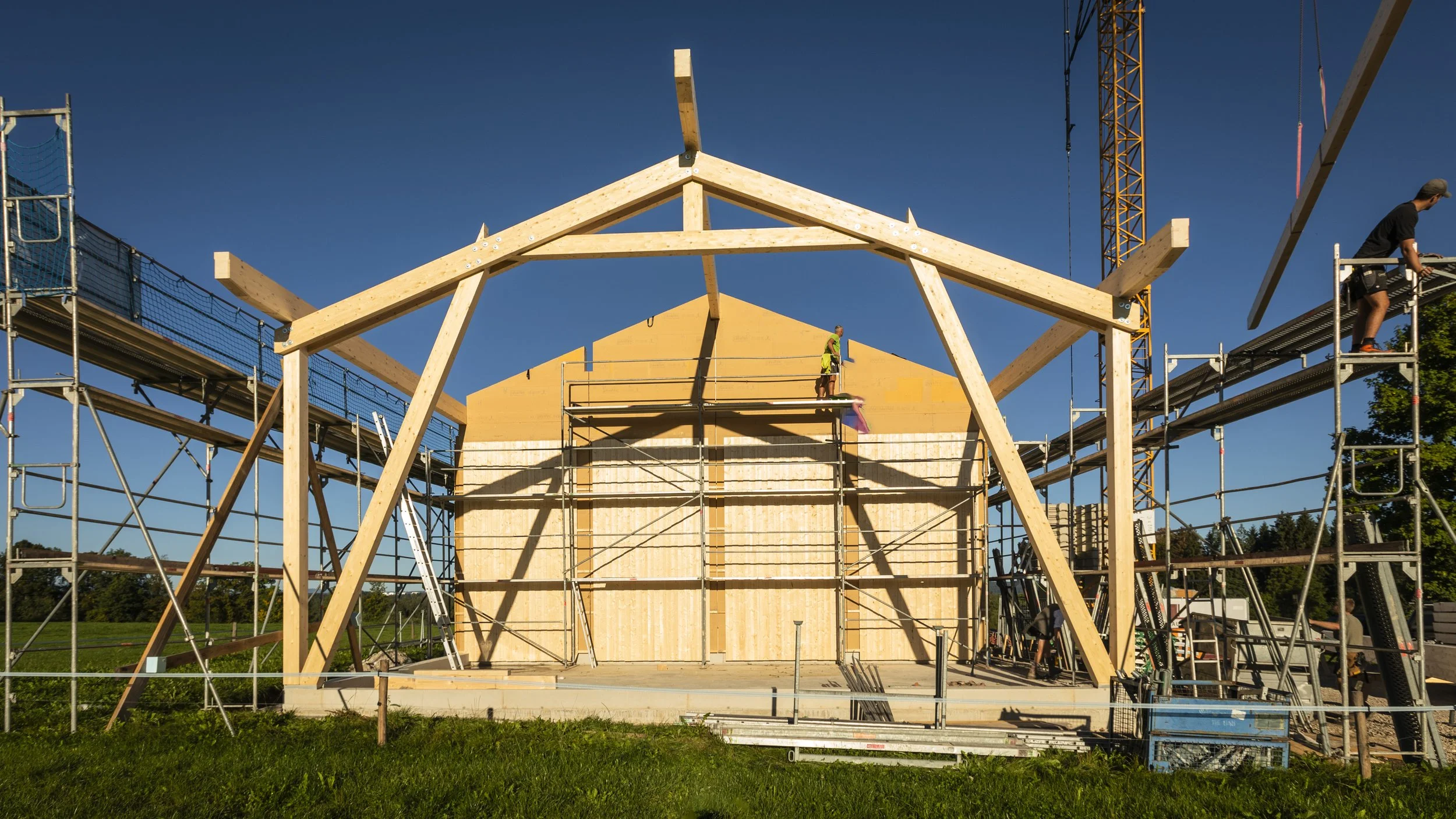 Bau eines Holzhauses mit Klettergerüst auf einer Baustelle bei sonnigem Himmel.