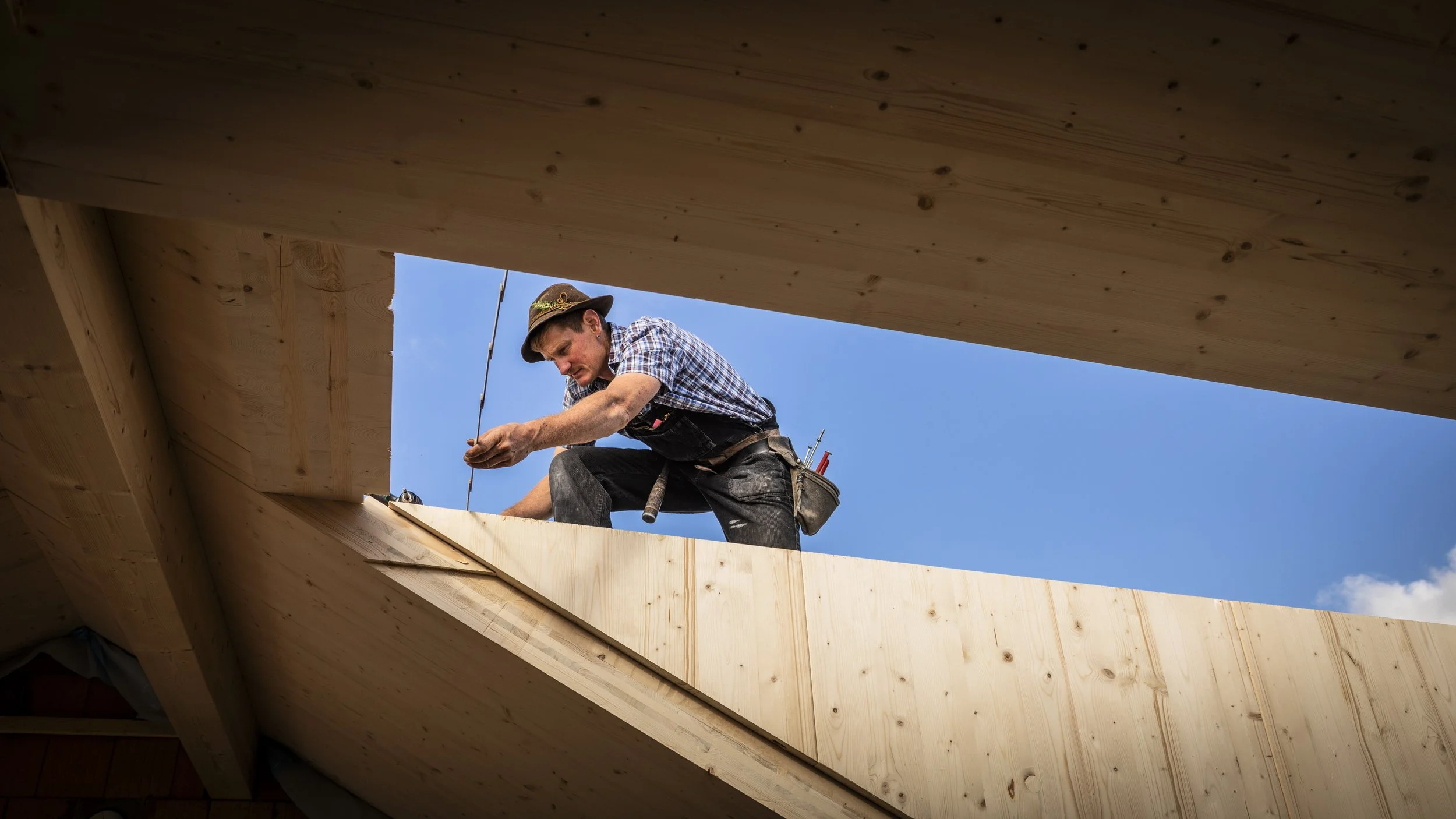 Ein Handwerker arbeitet auf einem Dach unter einem blauen Himmel, umgeben von Holzbauplatten.