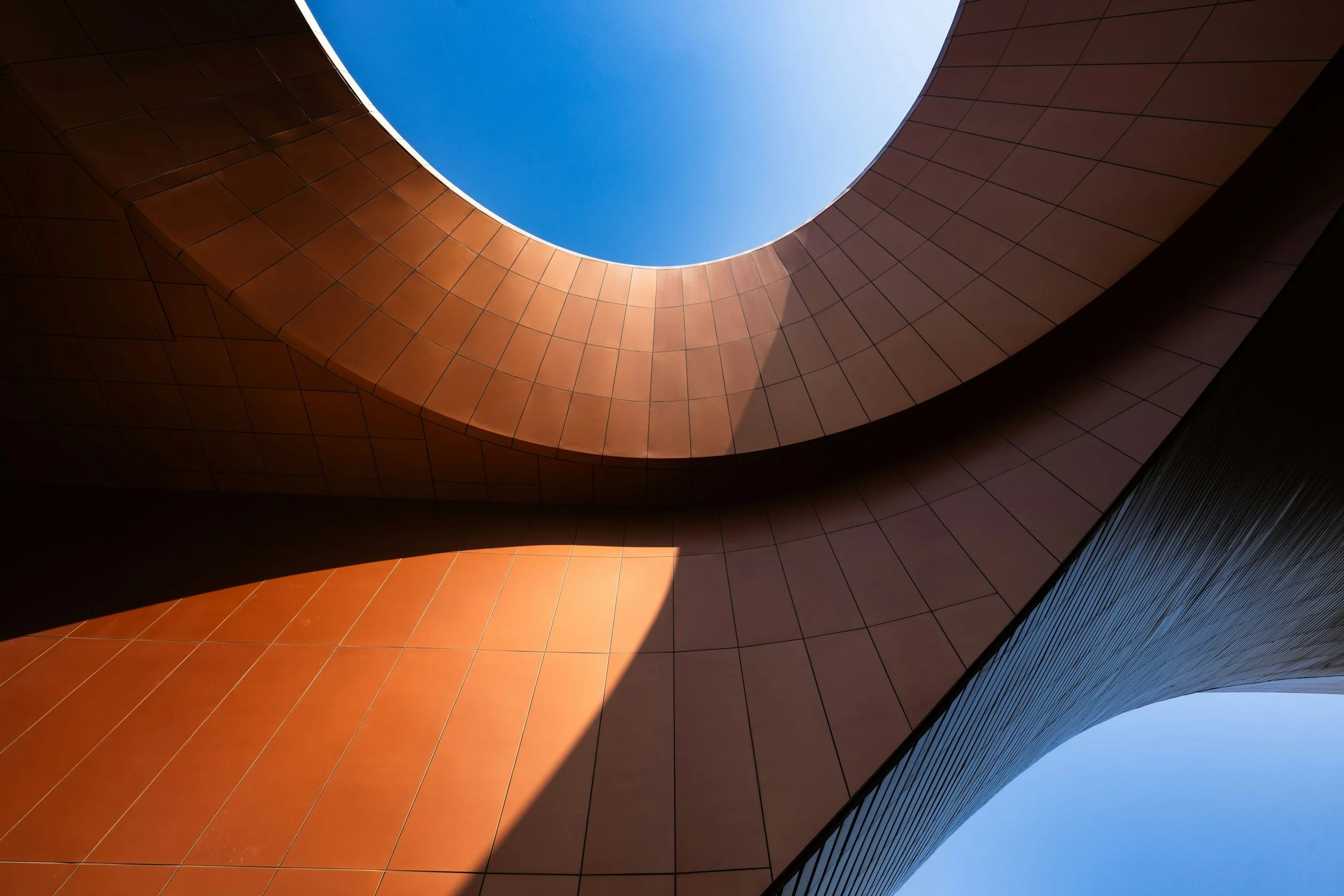 Looking up through an architectural opening with curved, tiled walls and blue sky visible above.