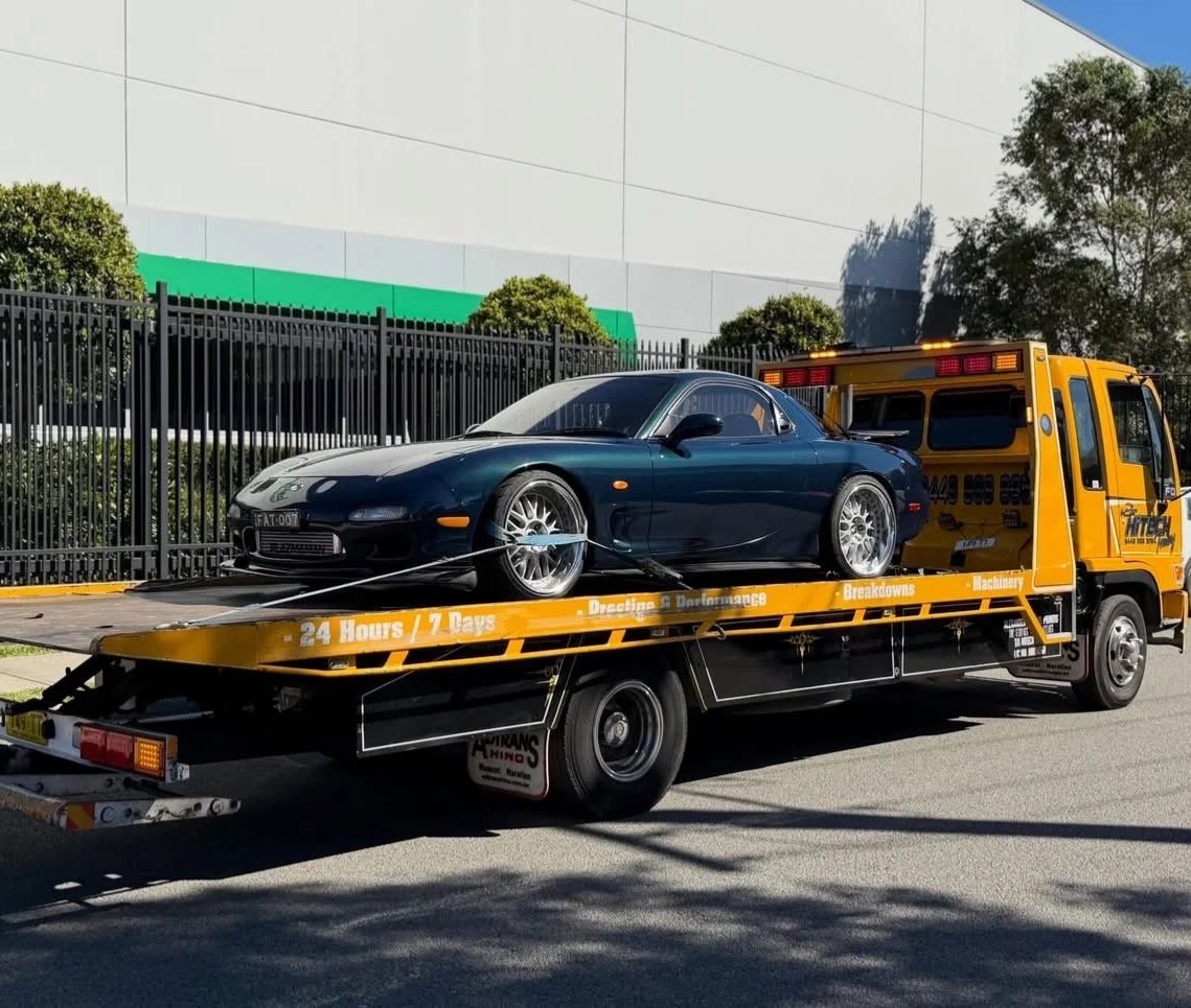 A black sports car loaded on a yellow tow truck in a parking lot.