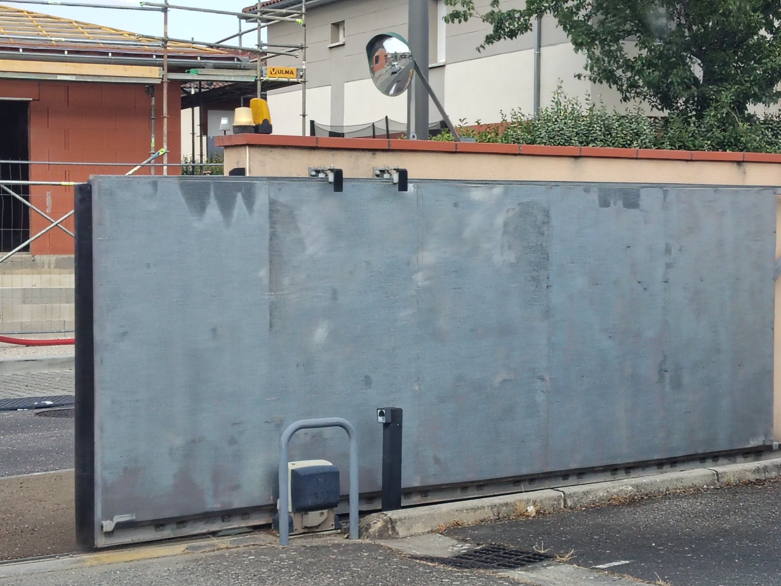 Mirroir convex fixé sur un mur, reflet de la rue avec une voiture, une maison et le ciel.