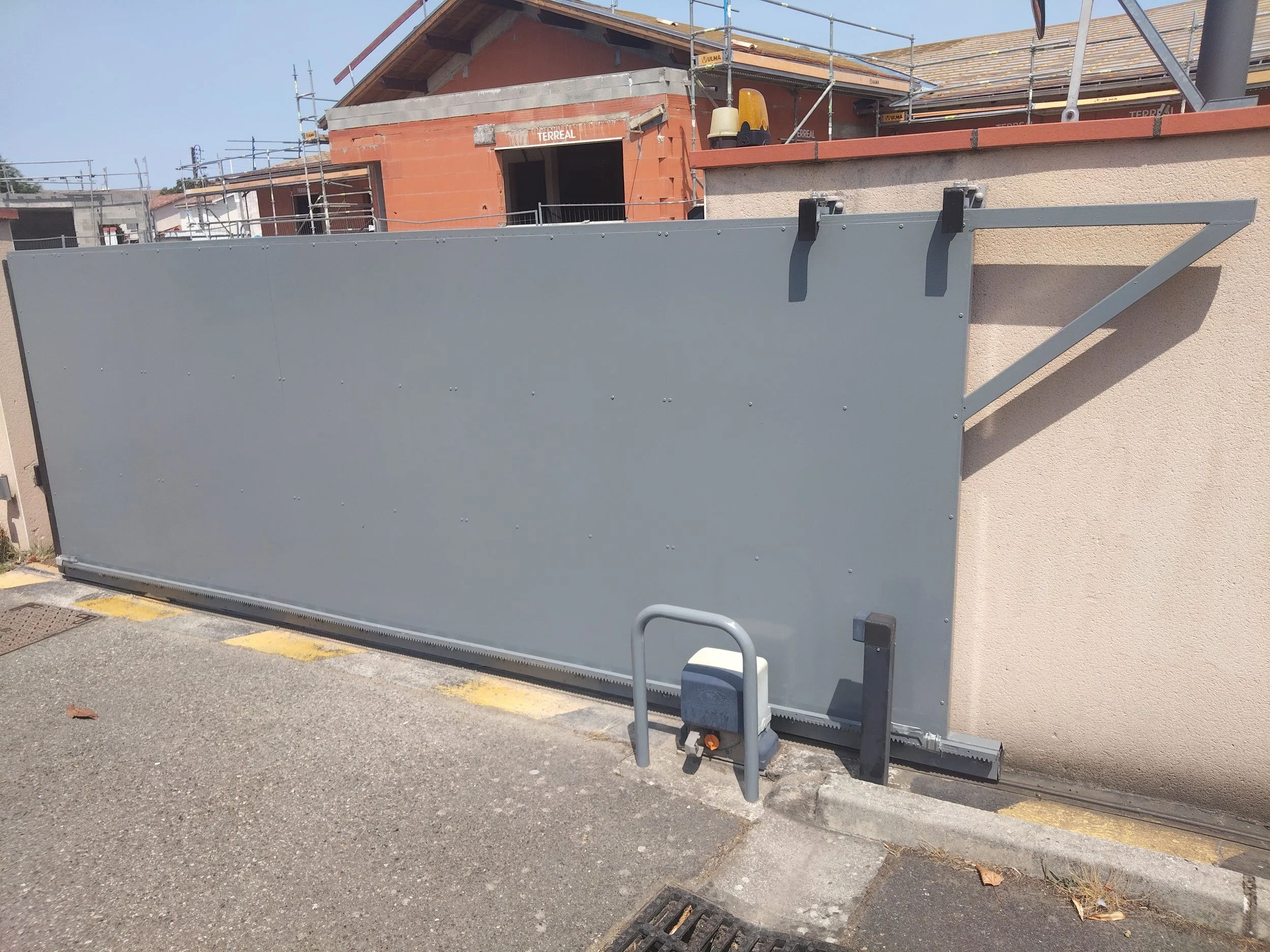 Une clôture en métal gris installée à l'extérieur d'un bâtiment en construction avec un toit en tuiles. Il y a des échafaudages autour de la structure en construction.
