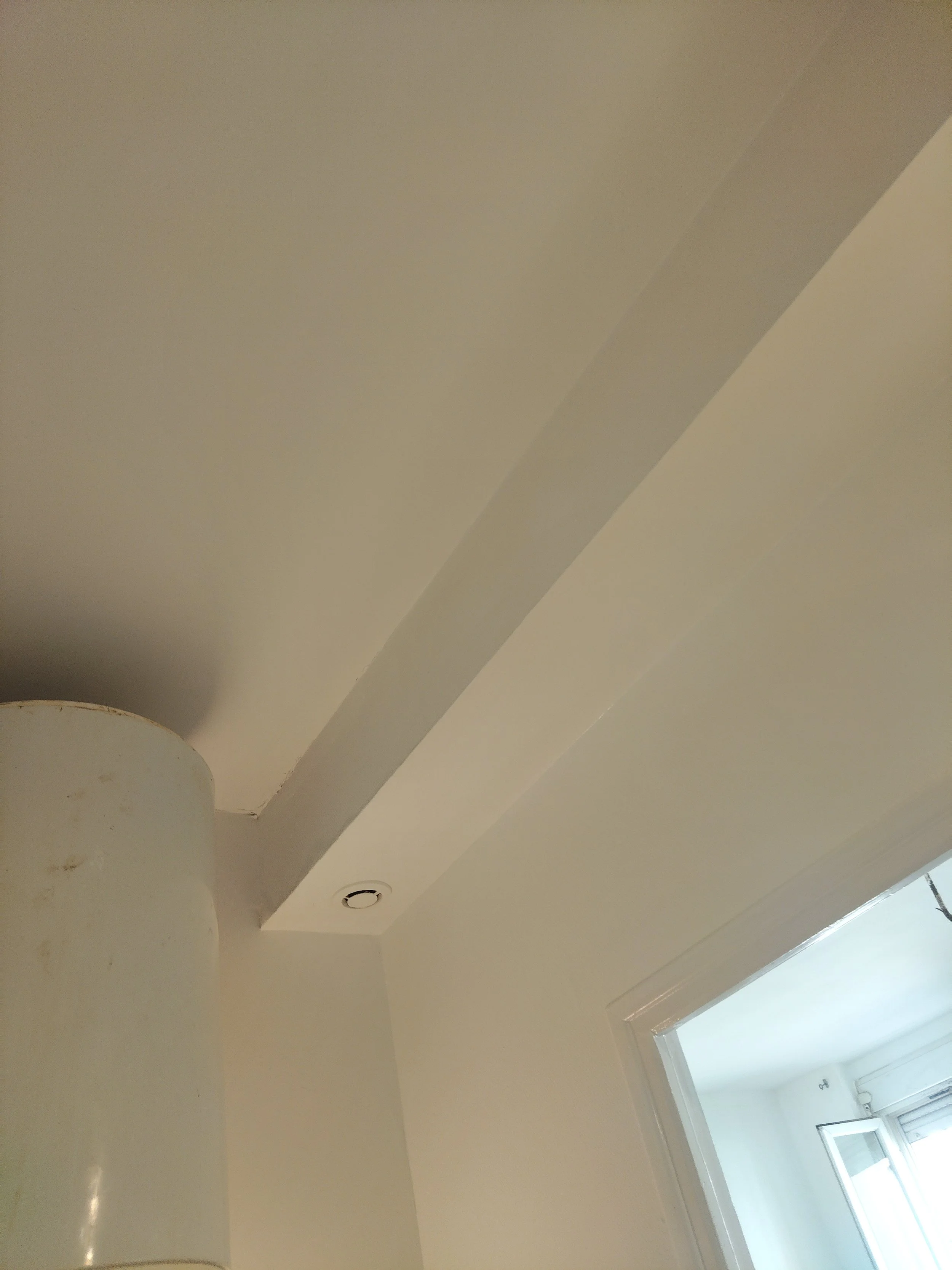 Plafond blanc avec deux spots encastrés et une porte fenêtre laissant entrer de la lumière.