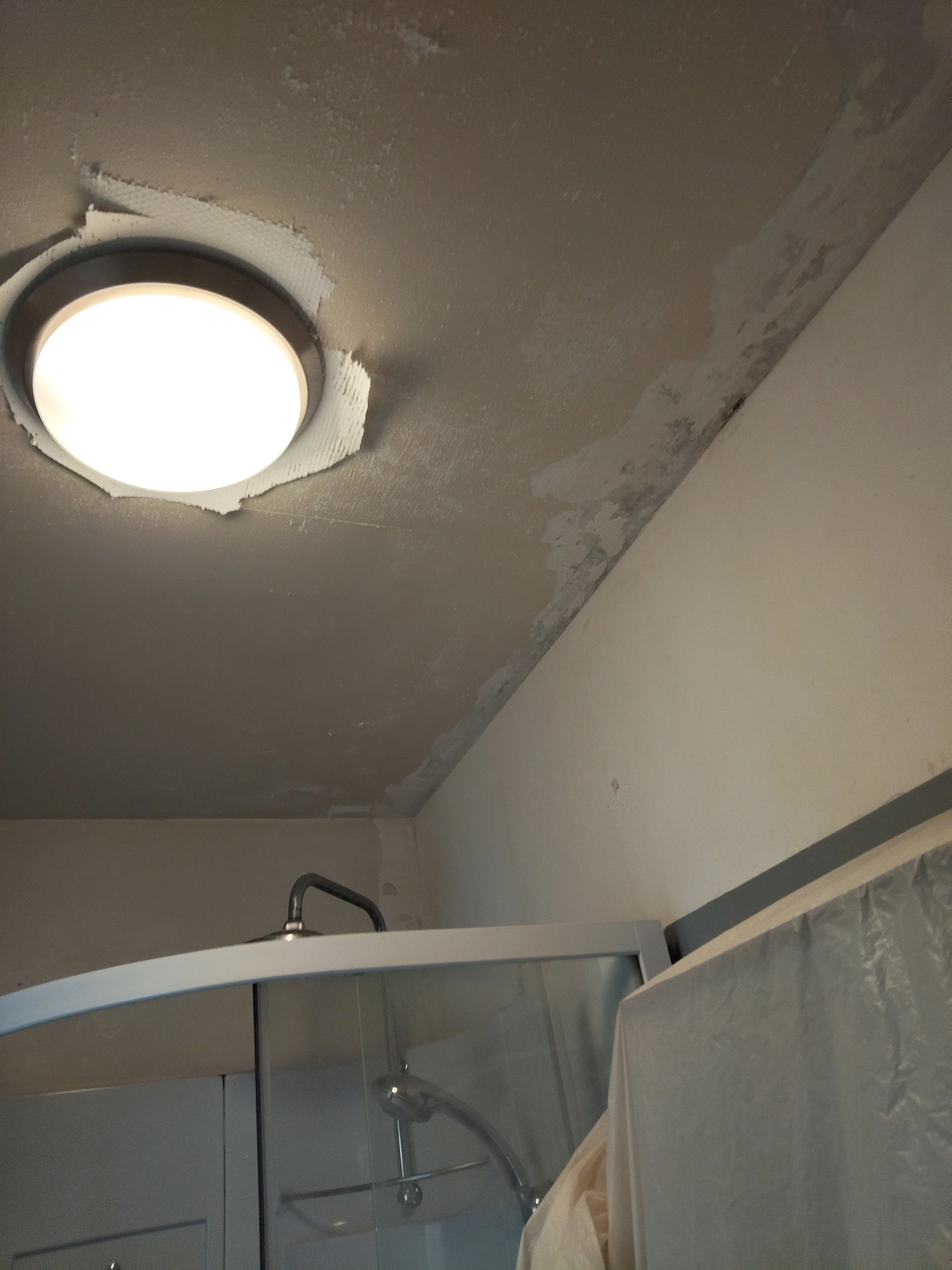 Une salle de bain en cours de rénovation avec un plafond partiellement peint, un éclairage rond encastré et des surfaces en mosaïque ou carrelage, avec un lavabo et un miroir.
