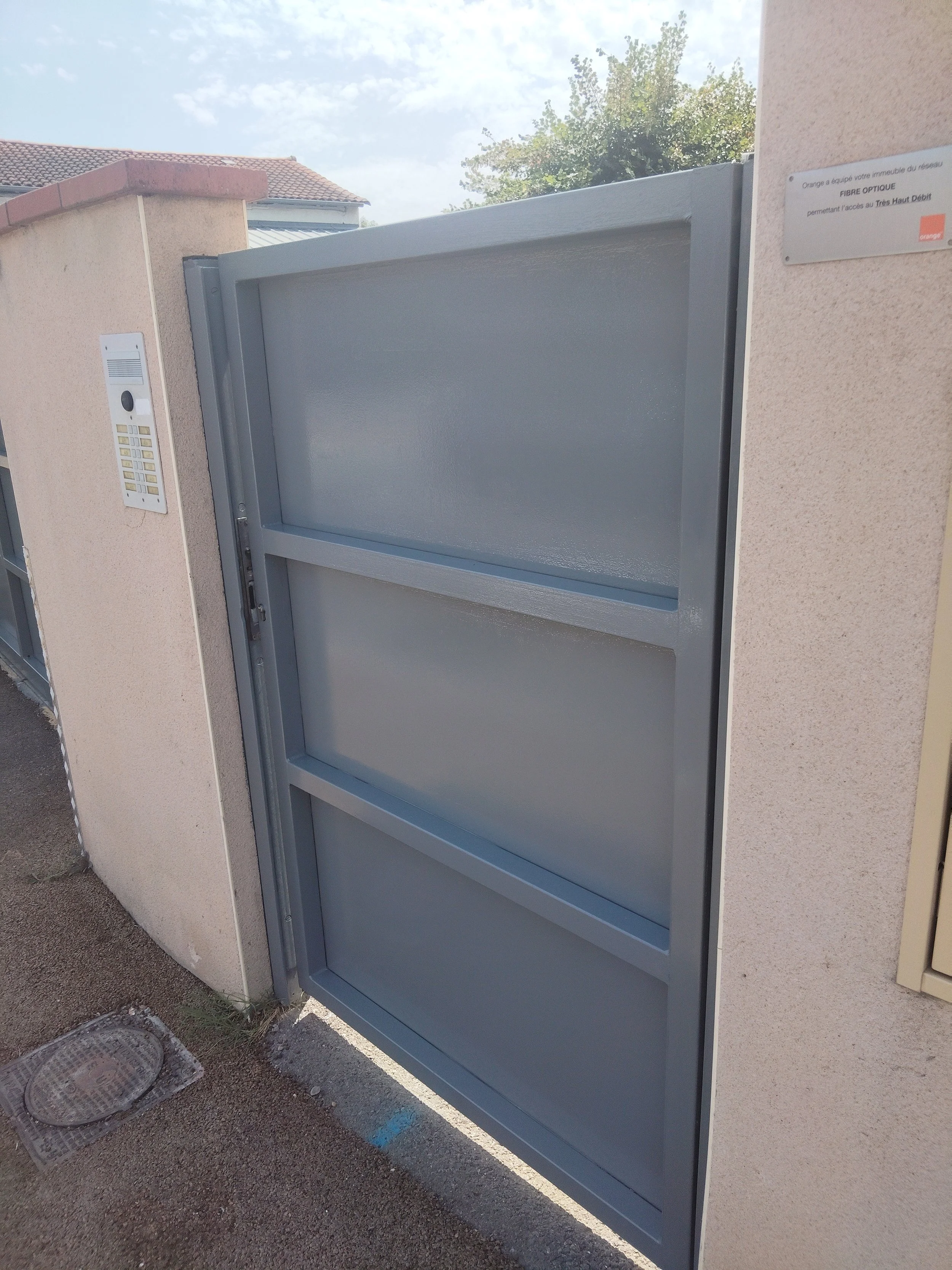 Une porte de bâtiment avec une interphone. Un panneau indique qu'il s'agit d'une fibre optique permettant l'accès à Très Haut Débit, avec la marque orange.