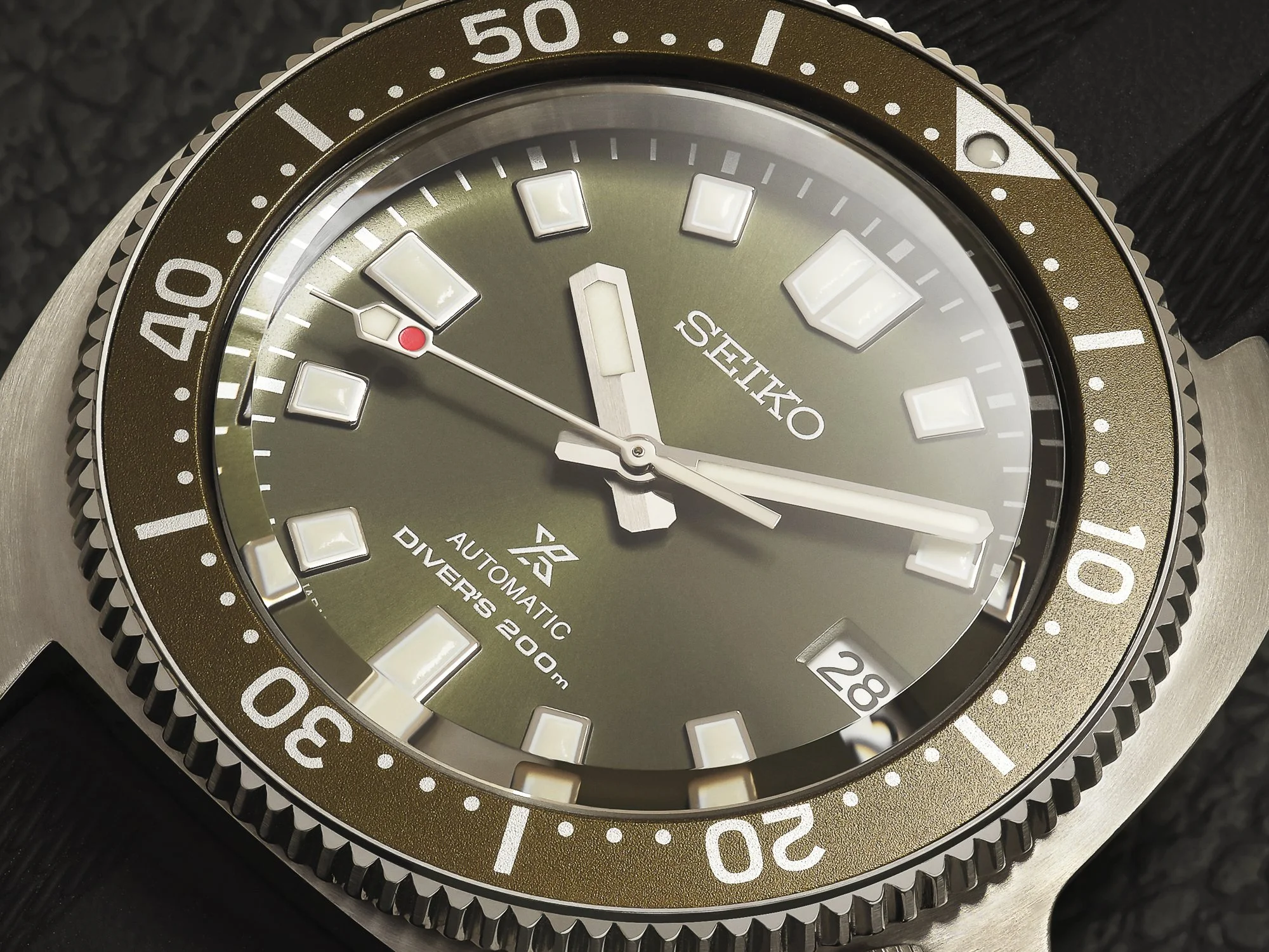 Een Seiko duikhorloge met een grijsgroene wijzerplaat, witte lumen wijzers, een datumvenster en een roestkleurige rand met witte markeringen.