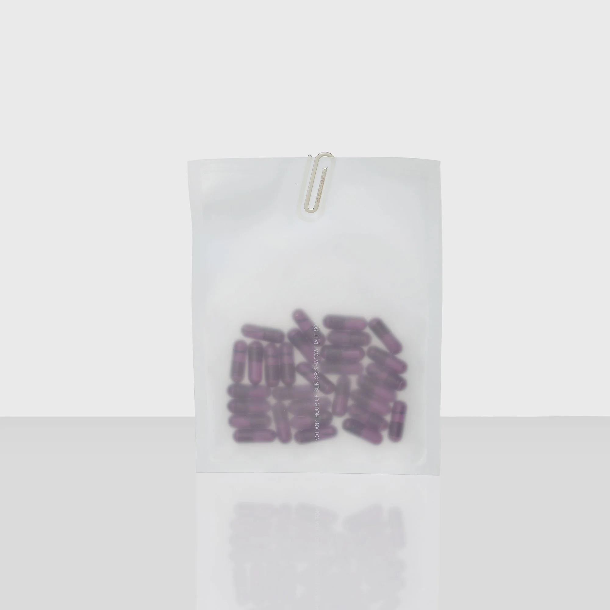 Een wit papier met een paperclip bovenaan, en onderaan een glazen kubus gevuld met roze capsules. Op de kubus staat minimale tekst.