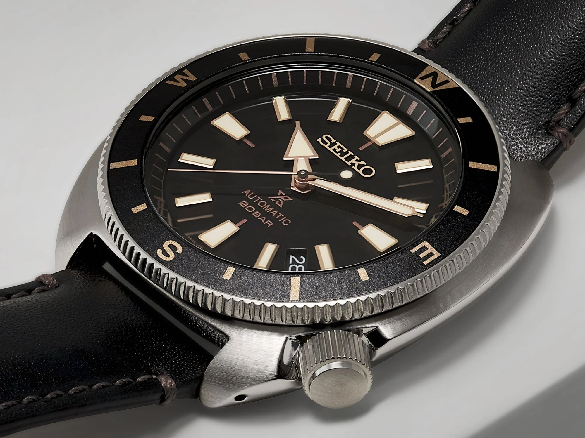 Dichtbij foto van een Seiko automatische duikhorloge met een zwarte wijzerplaat, gemerkt met 'Seiko', 'Automatic', '200 Bar' en een datumaanduiding, op een zwart leren horlogeband met stiksels.