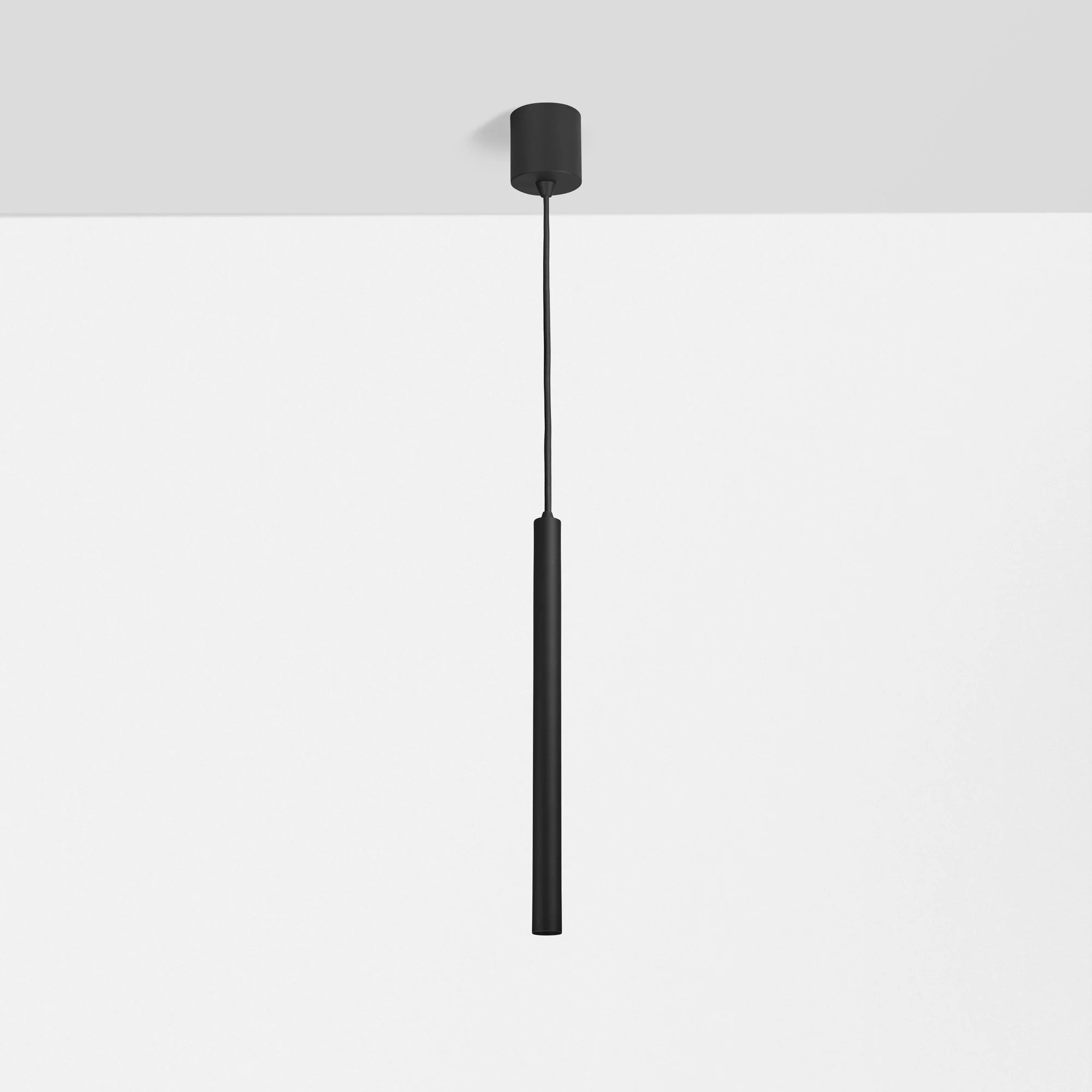 Een zwart plafondlamp met een lange stroomkabel hangt tegen een witte en grijze muur.