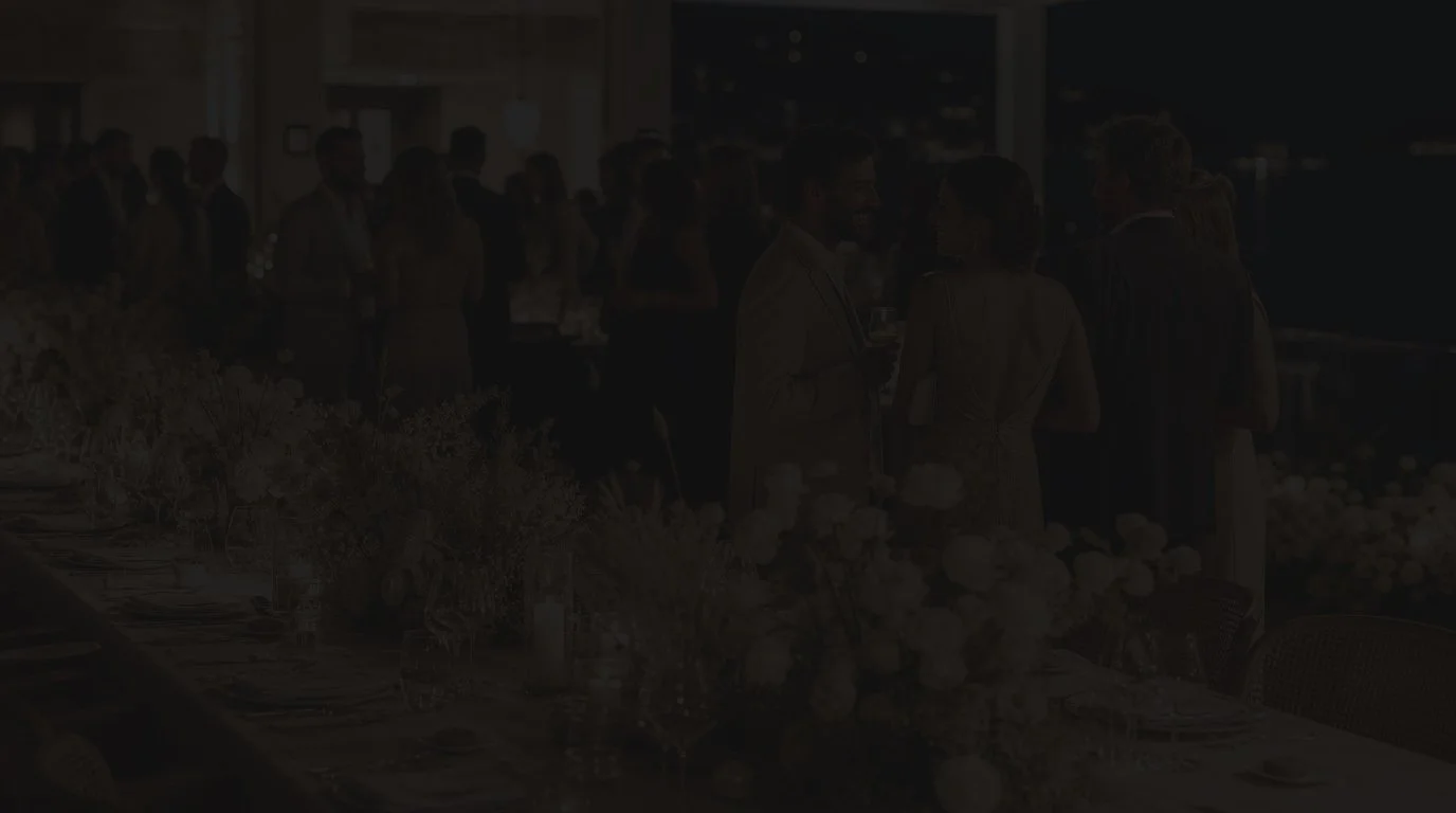 Invités élégamment habillés lors d’une réception nocturne avec tables dressées et décoration florale.