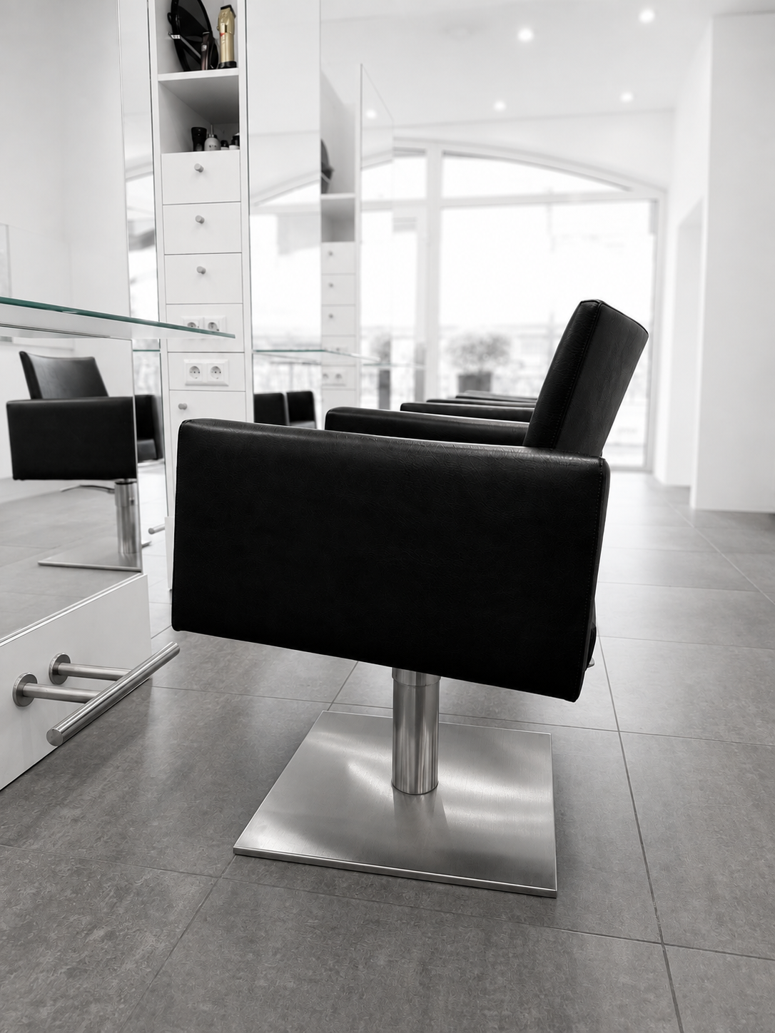 Omdat de afbeelding zwart-wit is, lijken de stoelen zwart en de ruimte modern en minimalistisch, met grote ramen en witte muren.