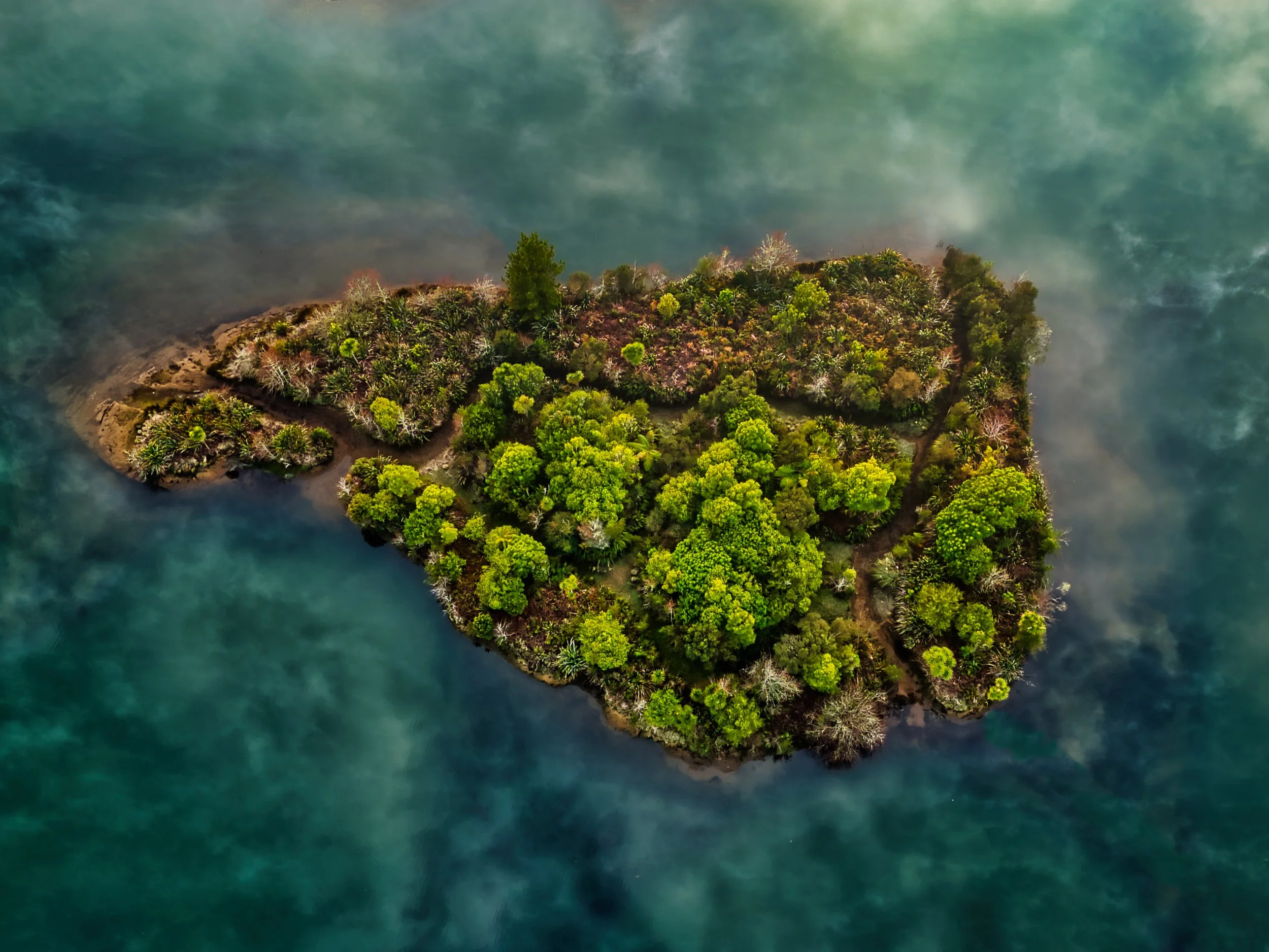 An aerial view of a small, lush green island surrounded by blue-green water with some fog or mist over the water.