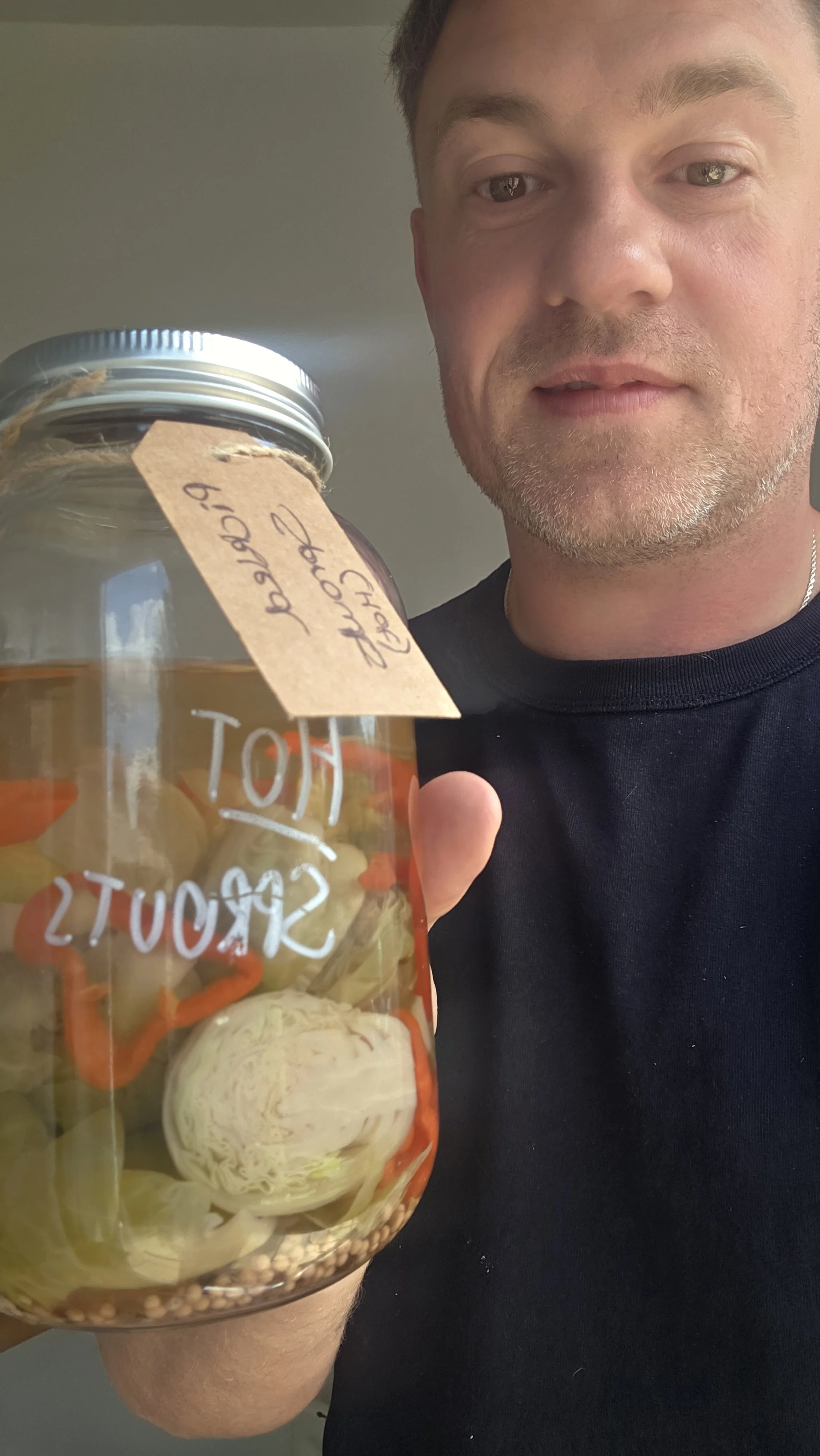 Rob holding a jar of Hot & Spicy pickled Brussels sprouts with a handwritten batch label
