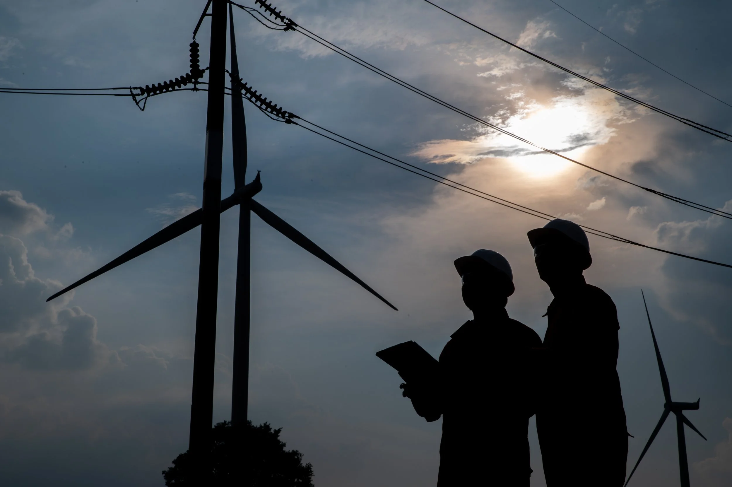 Utility field personnel reviewing electrical infrastructure near overhead power lines.