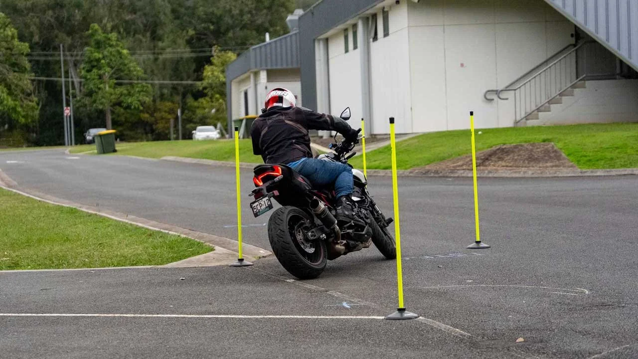 Motorcycle rider navigating around traffic cones in an outdoor parking lot or open area.