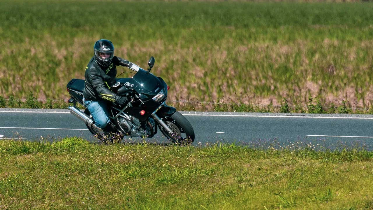A person riding a black motorcycle on a rural road surrounded by grassy fields.