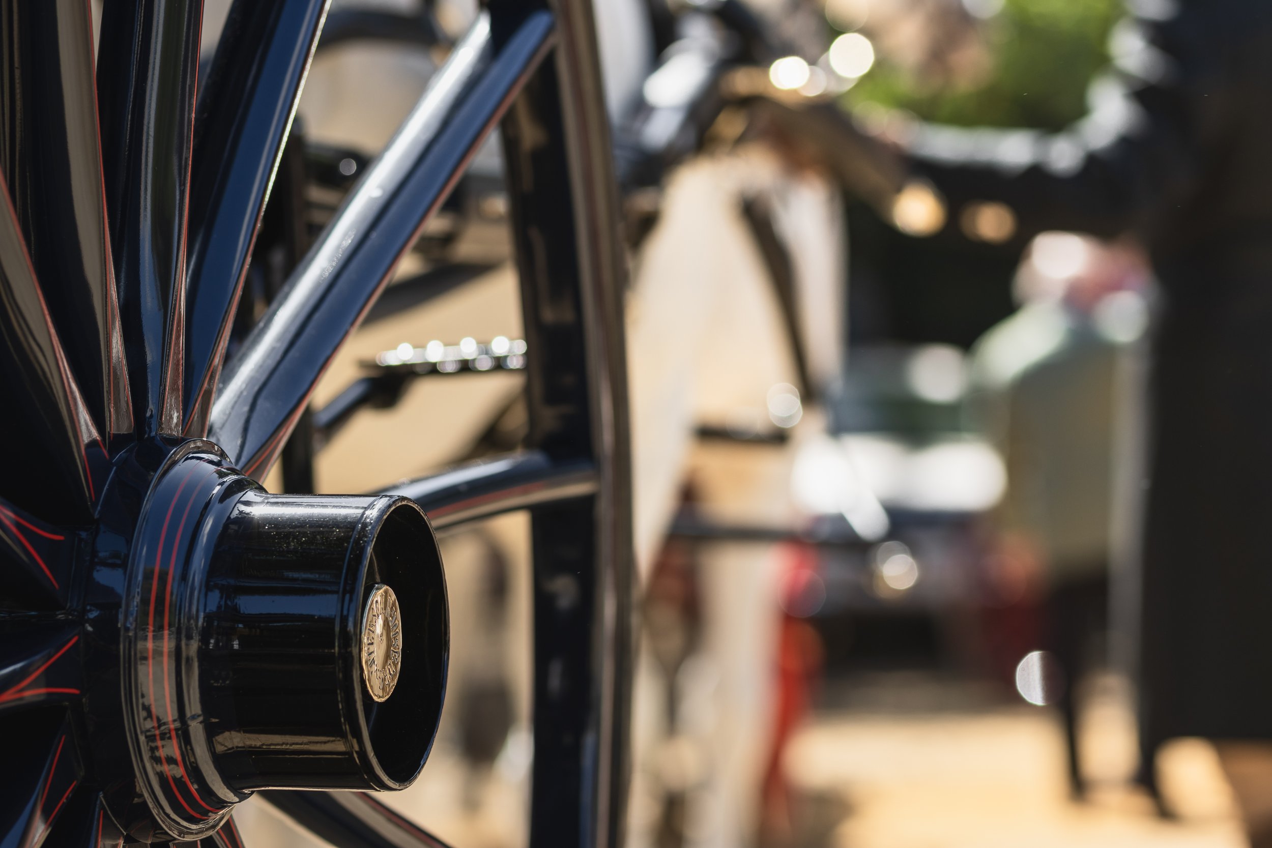 Close-up of a row of black bicycle rims with shiny spokes and hubs, parked outdoors on a sunny day.