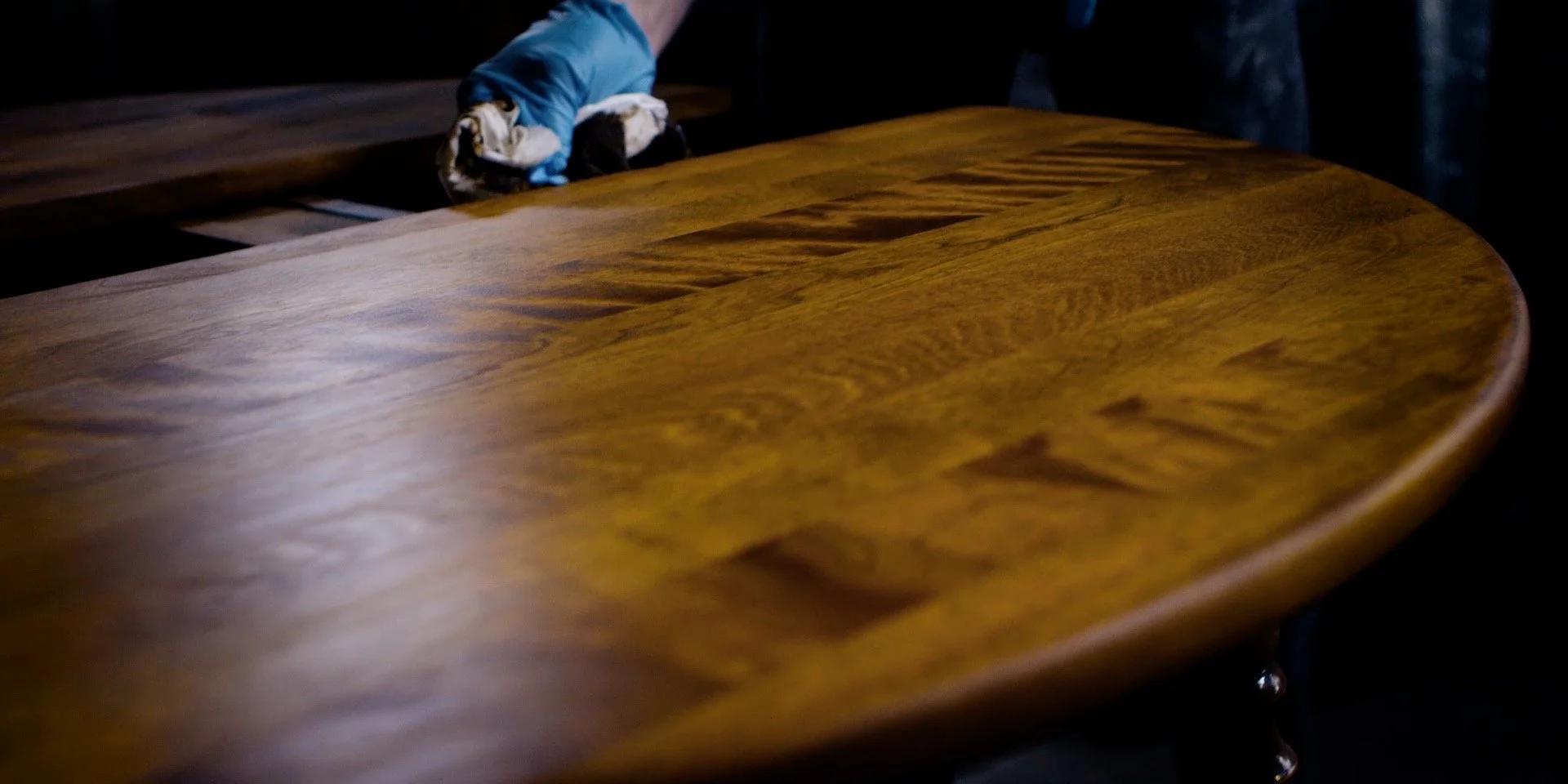 Chris Kunicki hand-finishing a wood dining table in his Denver furniture restoration workshop.