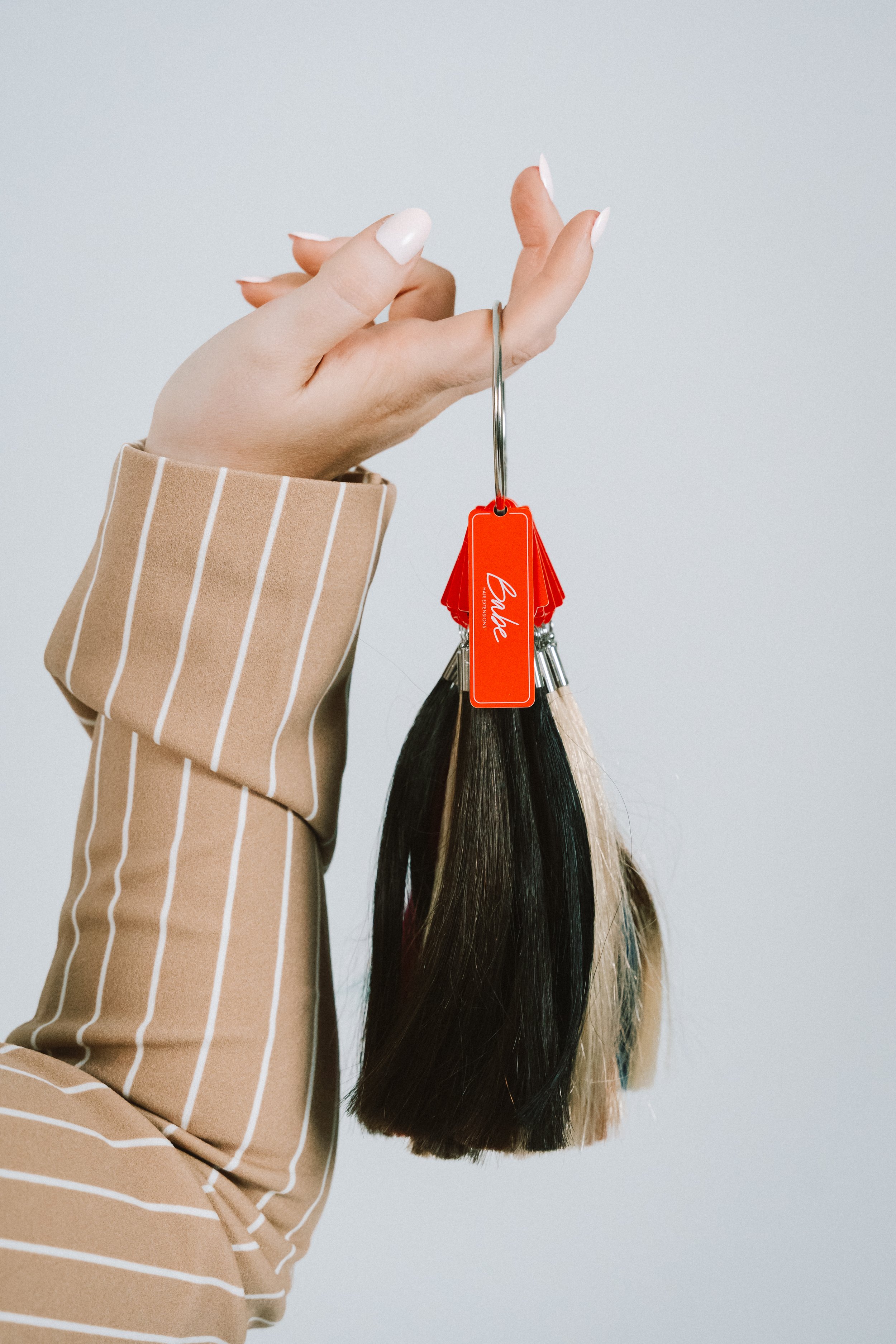 Hand holding a set of hair color swatches and hair extensions against a plain background.