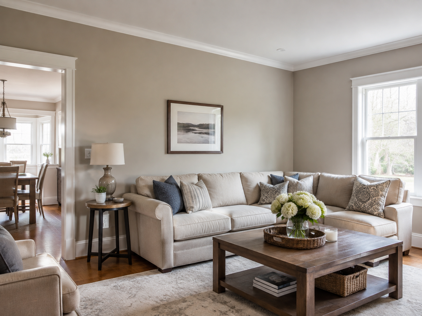 Living room with warm neutral walls, beige seating, a wooden coffee table, and an adjoining dining area.