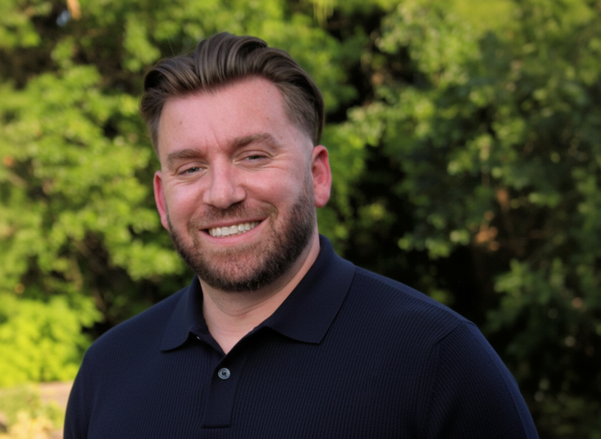 Patrick Pentalow, owner of Pentalow Property Services, with brown hair, beard, and blue eyes smiling outdoors with green trees in the background, wearing a navy blue polo shirt.