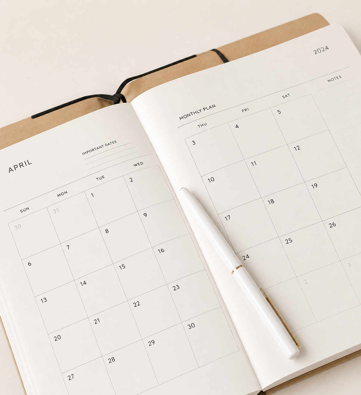 Open planner with calendar pages for April and May, with a white pen resting on it.