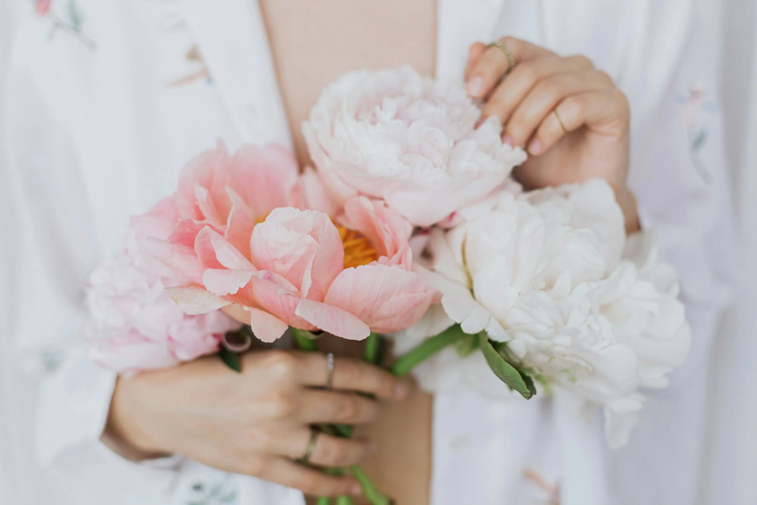 Hands holding pink and white peonies, a fresh, feminine feel for facials and beauty reset services in Santa Cruz