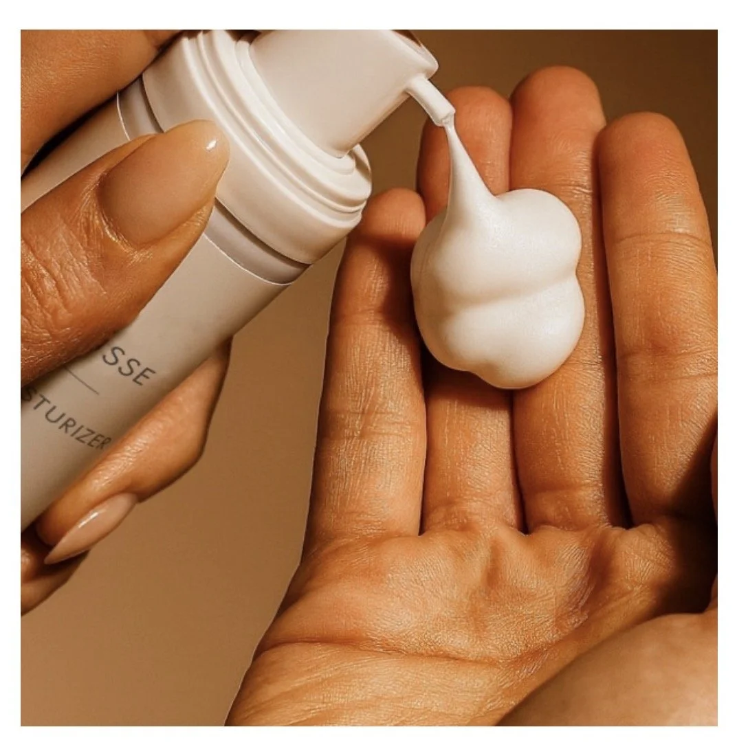 A person applying facial moisturizer or sunscreen to their hand from a white bottle.